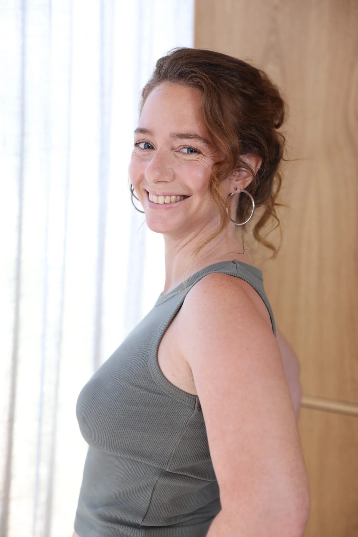 Photo of Rena staring and smiling at the camera with her hair in an updo and large, round silver earrings