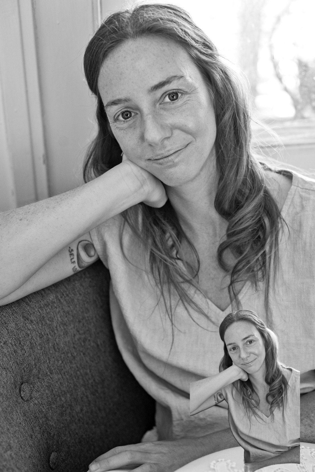 Black and white phot of Rena staring at the camera with a closed mouth soft smile with one hand on her neck