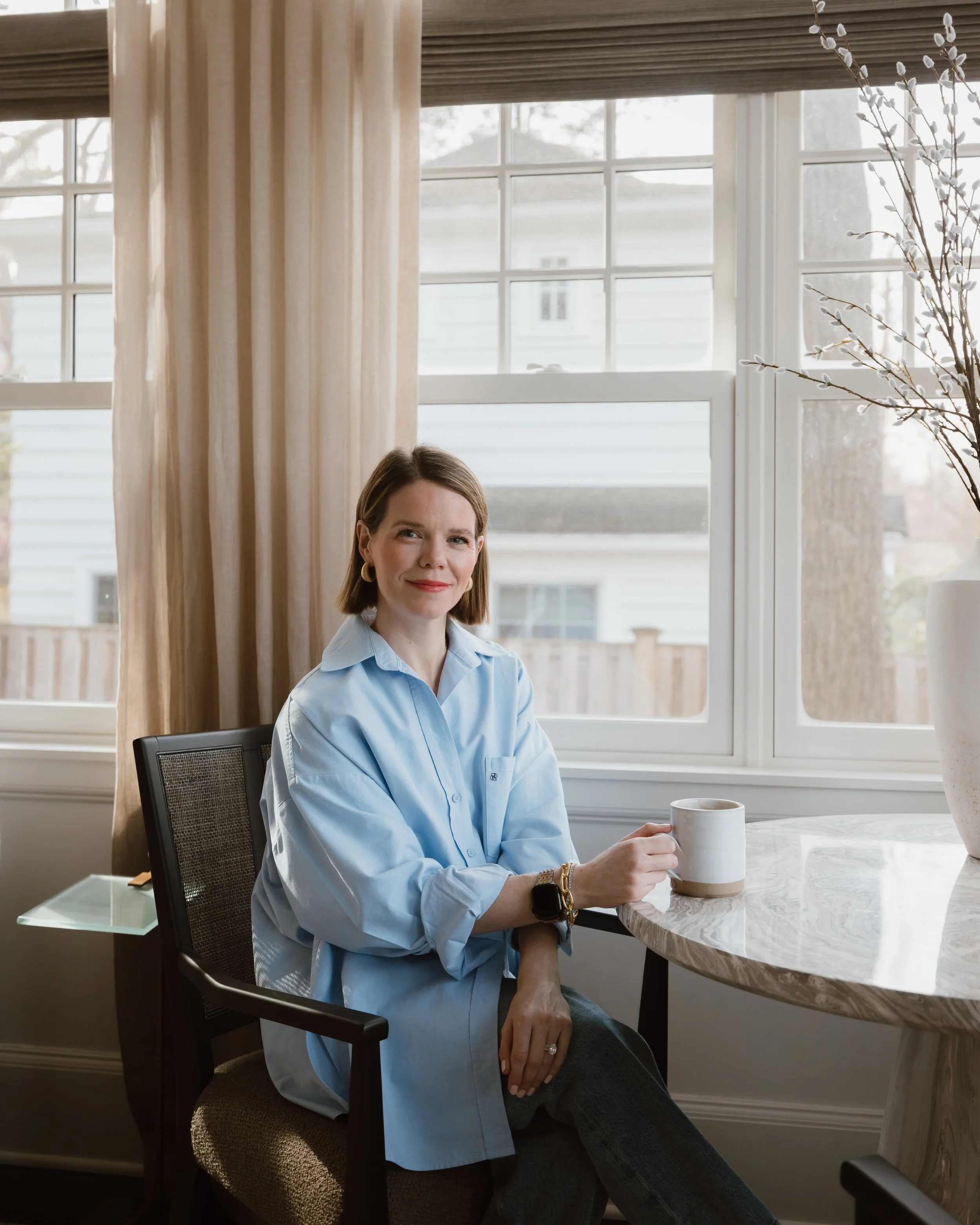 Image of Teresa Curtis, owner of Curtis Rowe Interiors.  Sitting in a blue button down shirt with a cup of cofee in her hand ready to take on your deisgn projects.