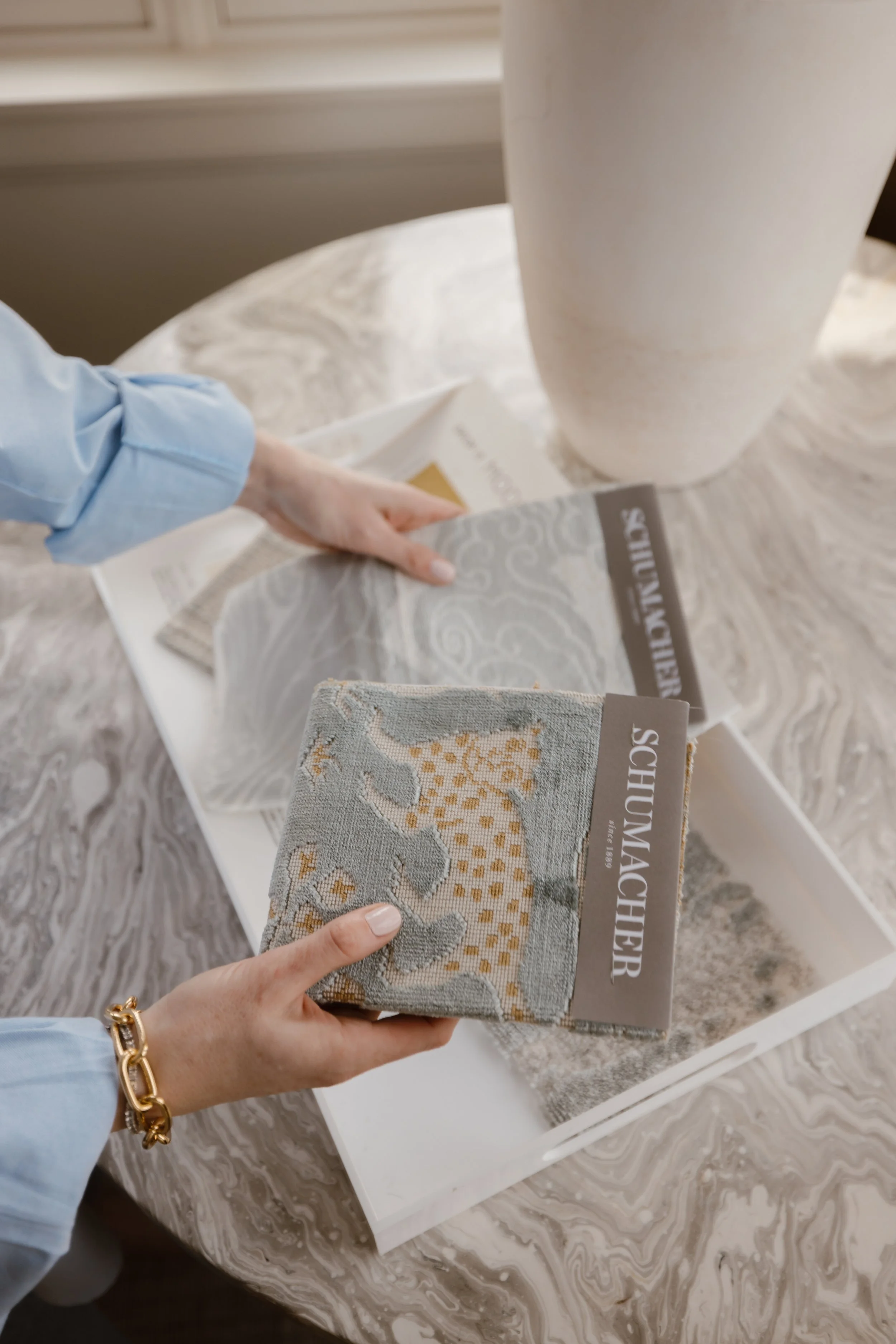 Hands holding fabric samples labeled 'TEXTILE SURFACE' and 'FRENCH TEXTILE' with a marble-patterned table in the background.