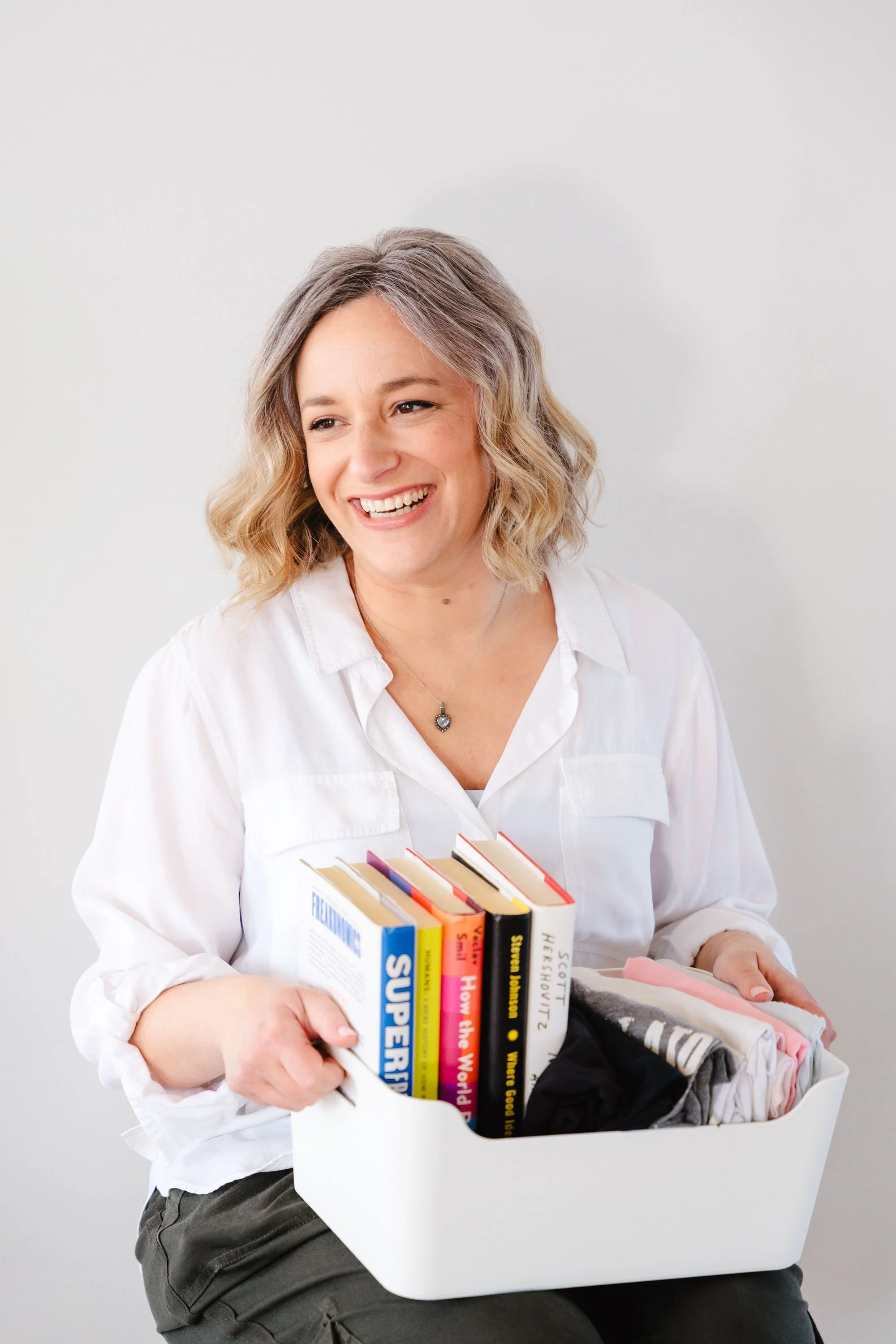 Corrie, the owner and professional organizer, smiling and holding a minimalist organizing bin with items inside