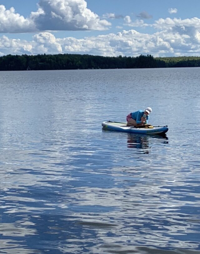 Jane at lake on paddle board taking water photos.jpeg