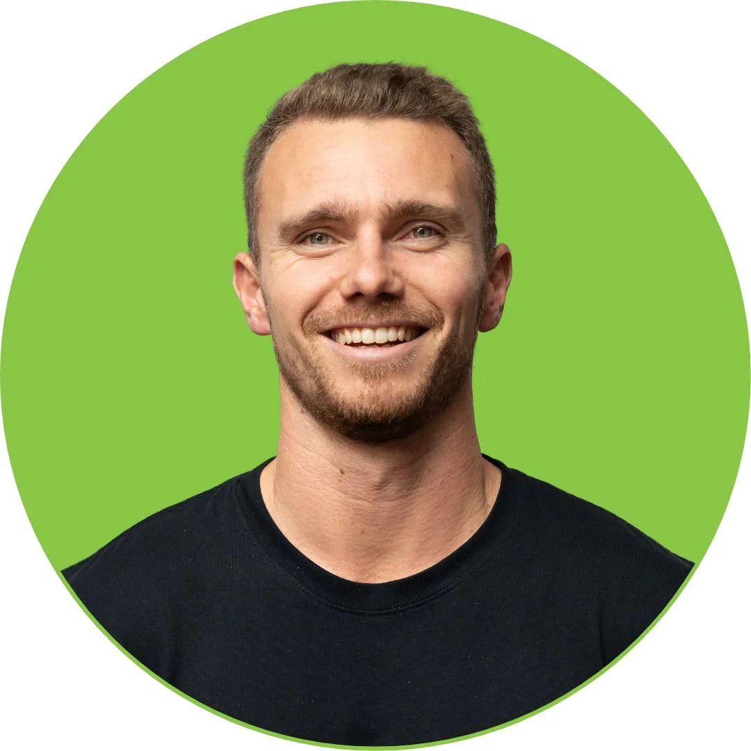 A smiling man with short brown hair and light facial hair, wearing a black t-shirt, against a bright green circular background.