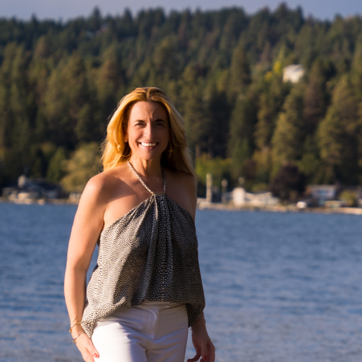 Nathalie Botros by a lakeside wearing a sleeveless top.