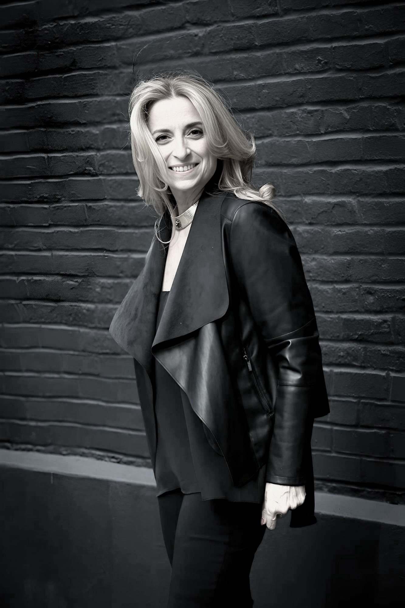 Nathalie Botros standing in front of a dark brick wall, wearing a black leather jacket.