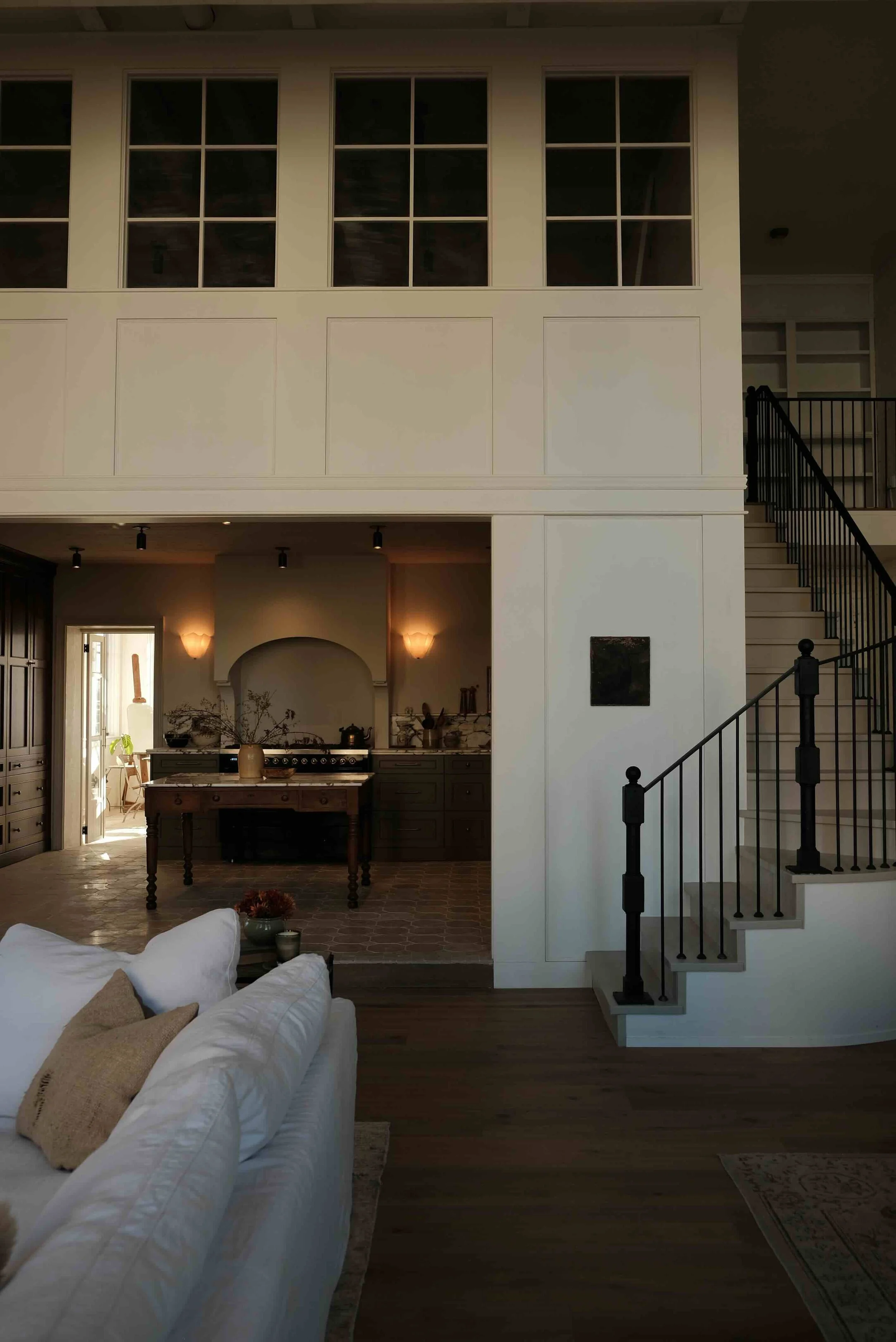 Interior of a two-story home with a staircase, kitchen area, and living room with white sofa and pillows.