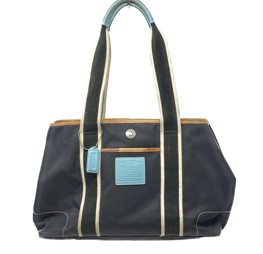 The Coach bag pictured here features striking light blue leather accents, tan trim, and striped canvas shoulder straps.