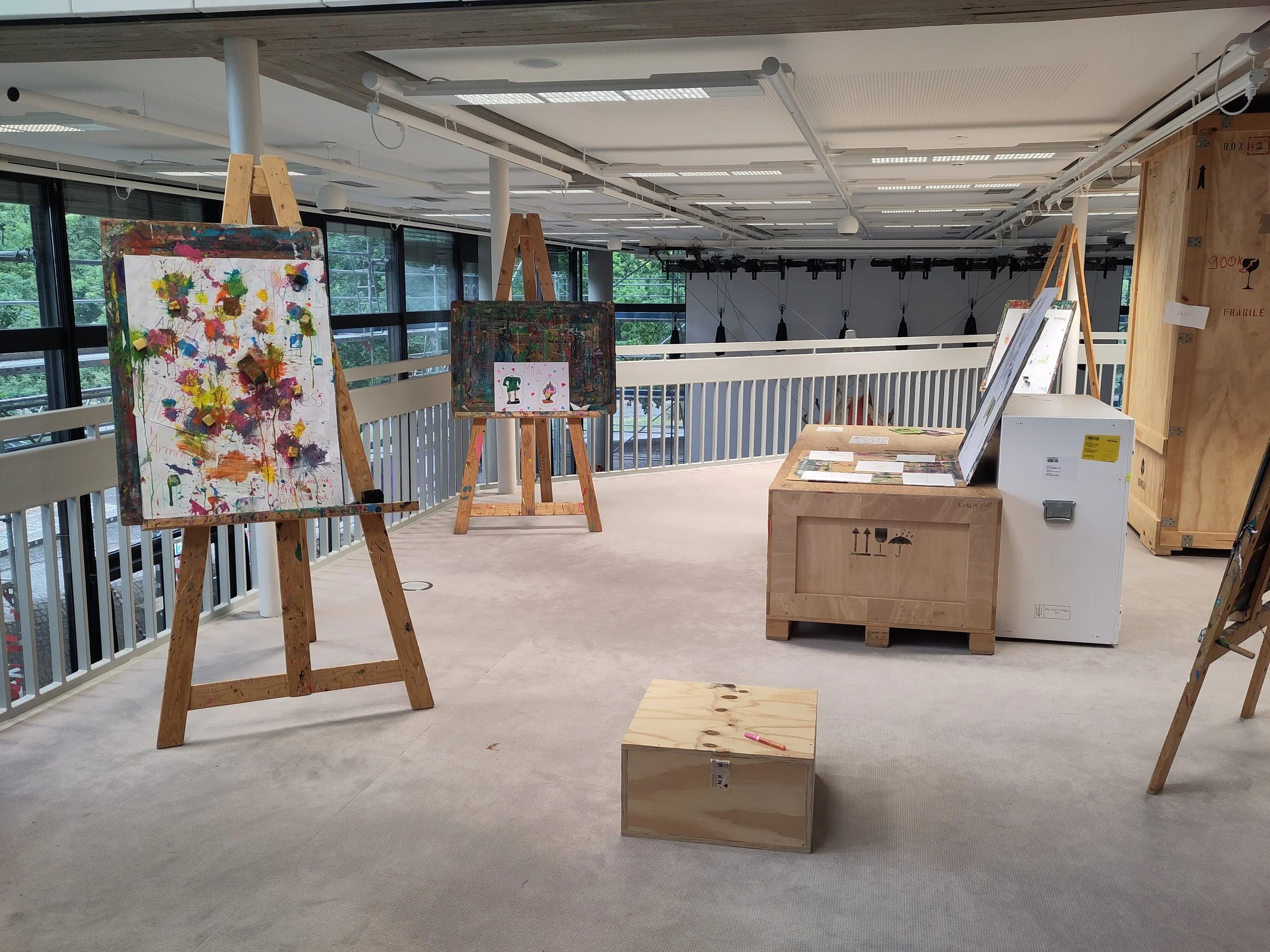 Staffelein mit bunten Farbexplosionen und zweichnungen, zwischen einer Installation aus Kunst-Versand-Kisten.