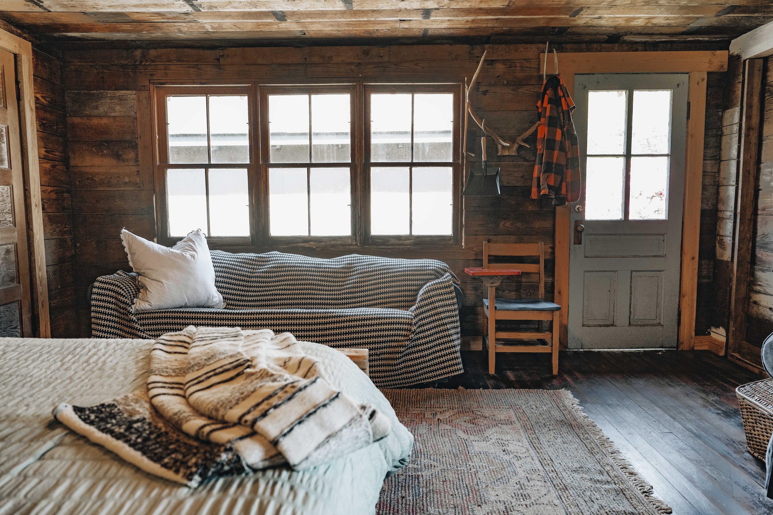 a very rustic room with wooden walls and ceilings, and rustic textiles on the bed.