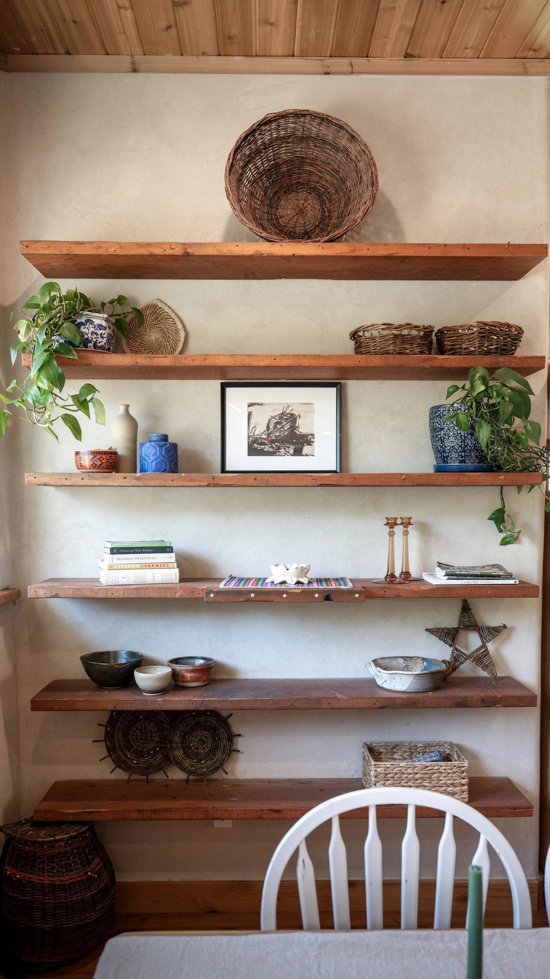 Custom wood shelving in the dining area of the handcrafted straw bale home, displaying willow baskets, pottery, and natural décor at Be Easy Farm in Sequim, Washington.