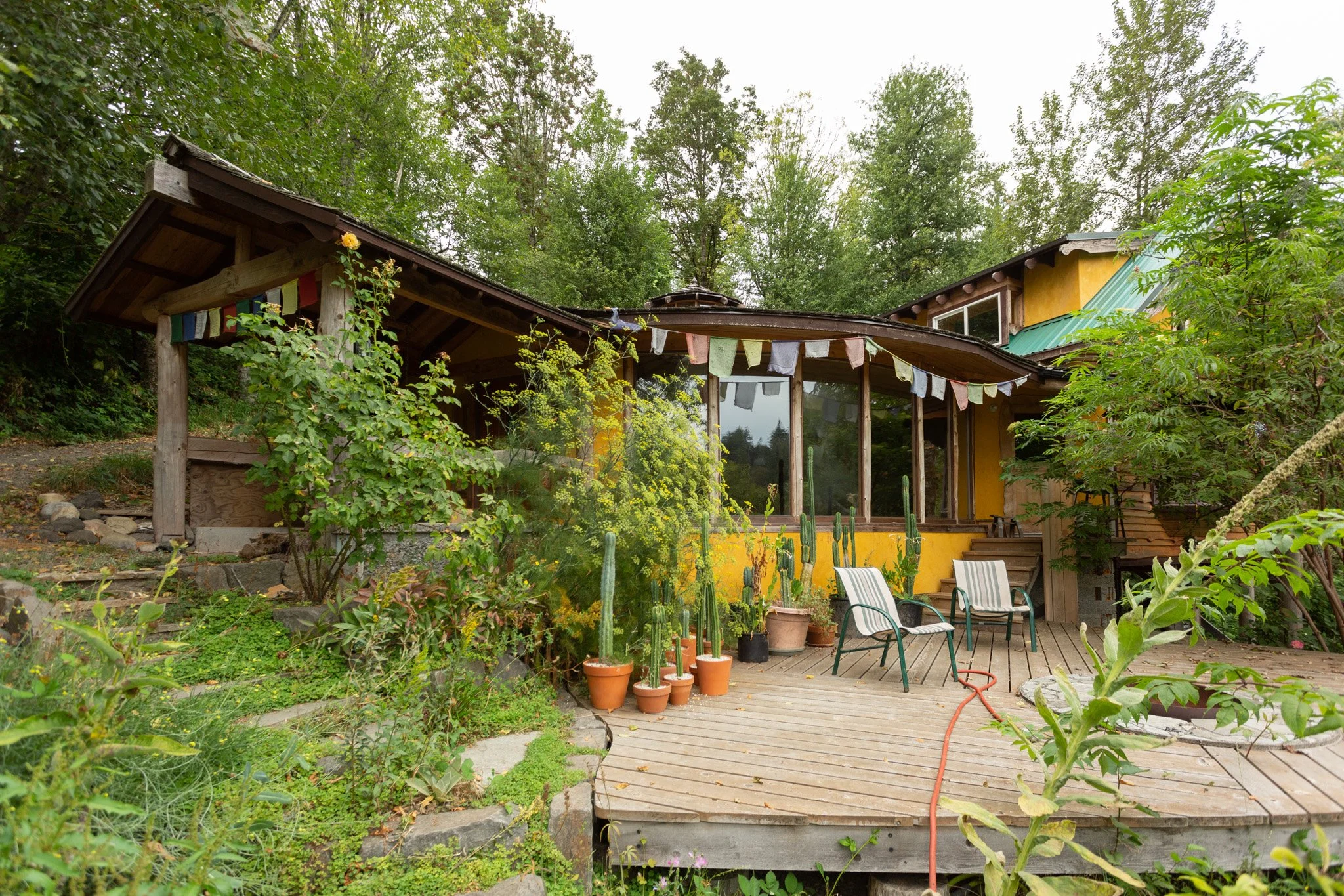 A lush front patio with a deck, fire pit, and lots of vegetation