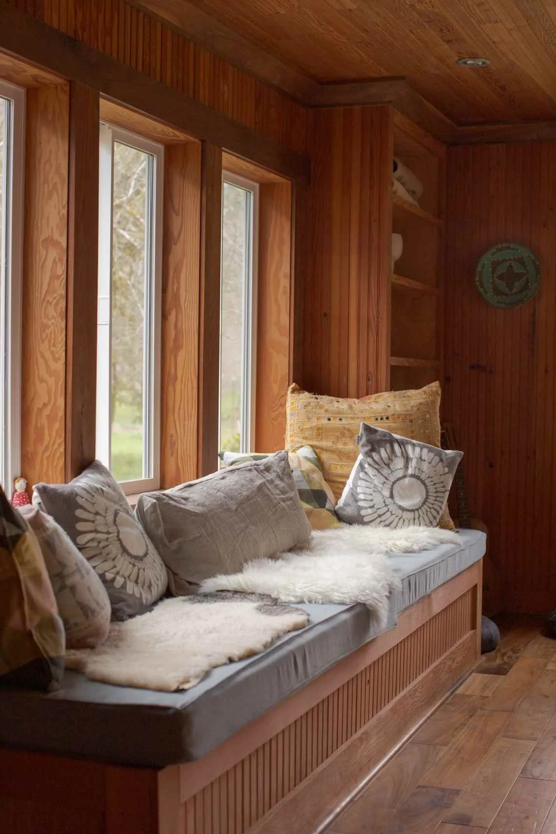Crafted wooden bench beside large farmhouse windows with rustic pillows, throws, and natural textures.