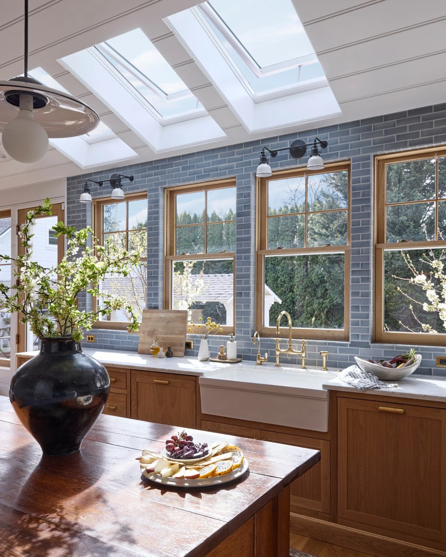A bright, cozy kitchen with brown wood cabinets, a blue backsplash surrounding four windows, and three Velux skylights in the ceiling.