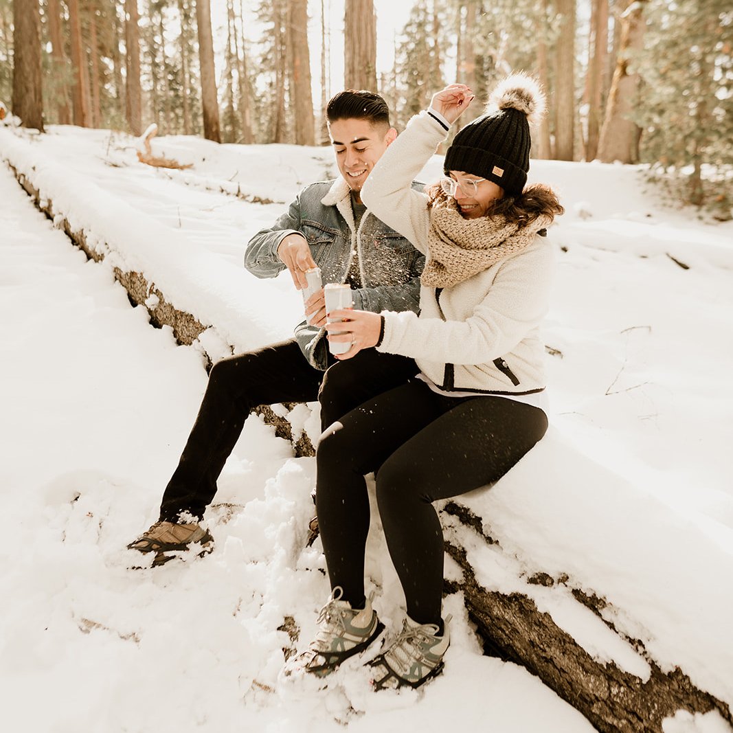 Couple having drinks and sitting on a log in the snow in Yosemite
