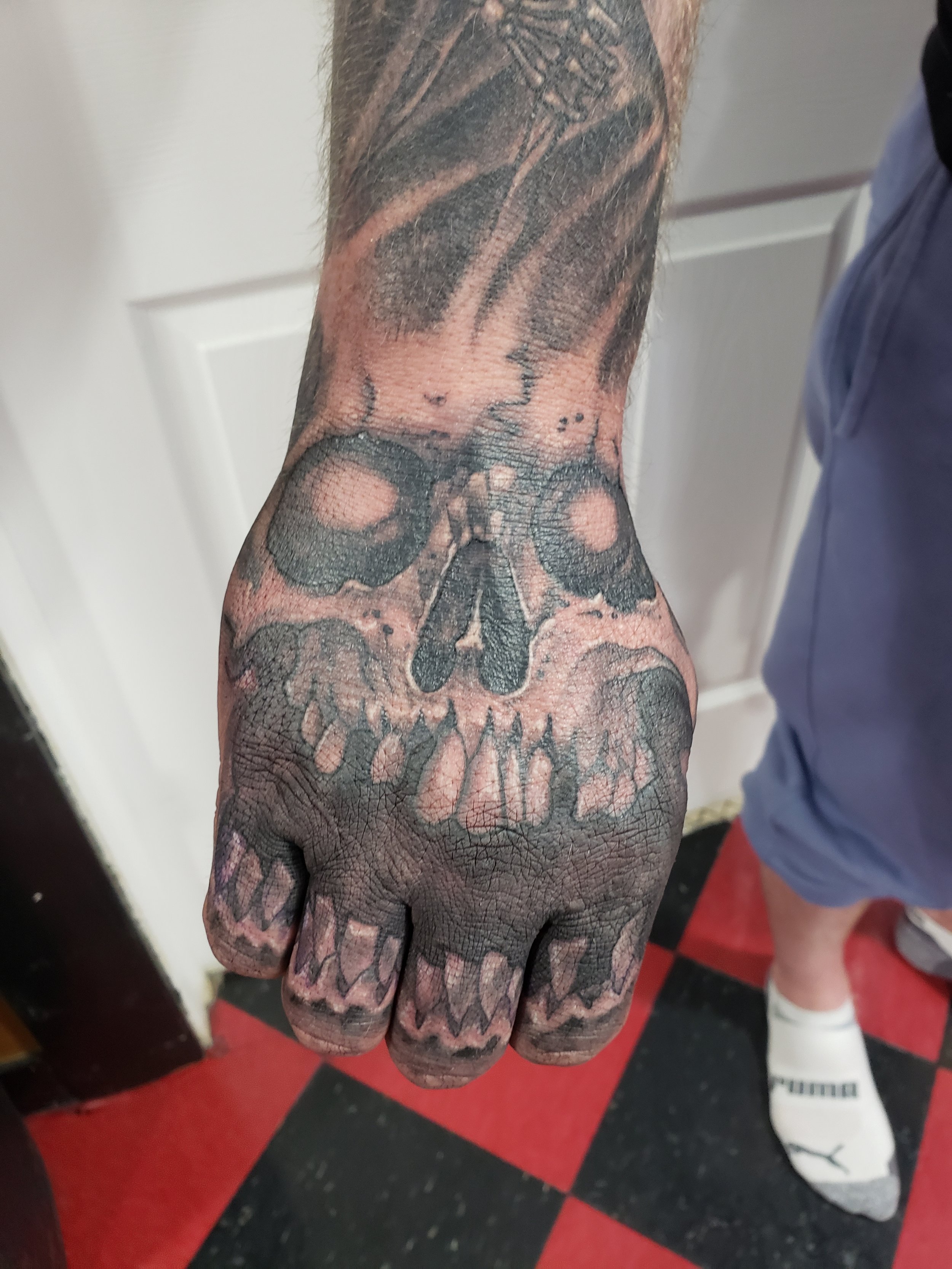 A person's arm with a large tattoo of a skull and a woman's face on the hand, in black and gray ink.