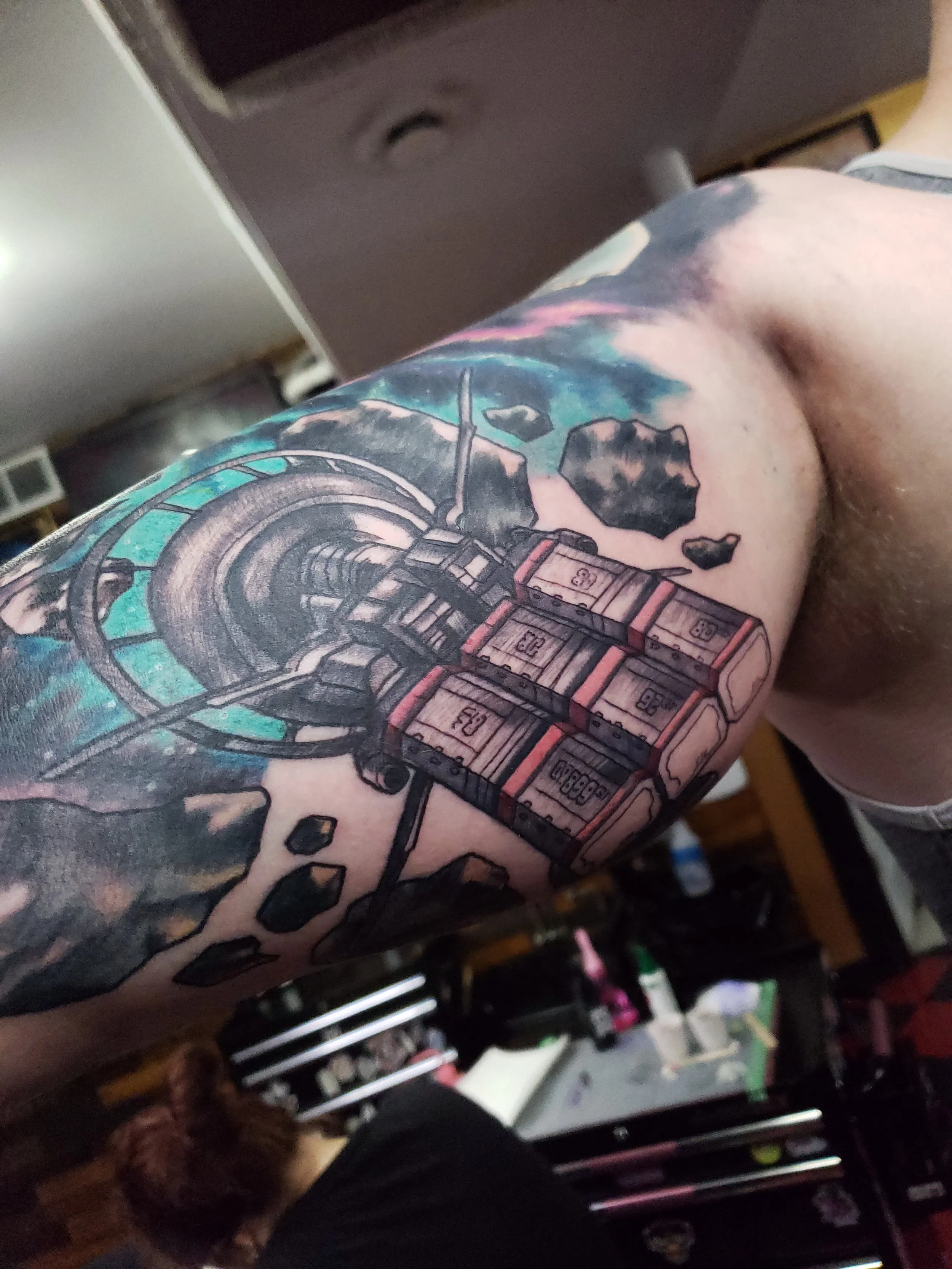 A person's arm with a colorful tattoo featuring a rocket and planets, and floating rocks around a space scene.