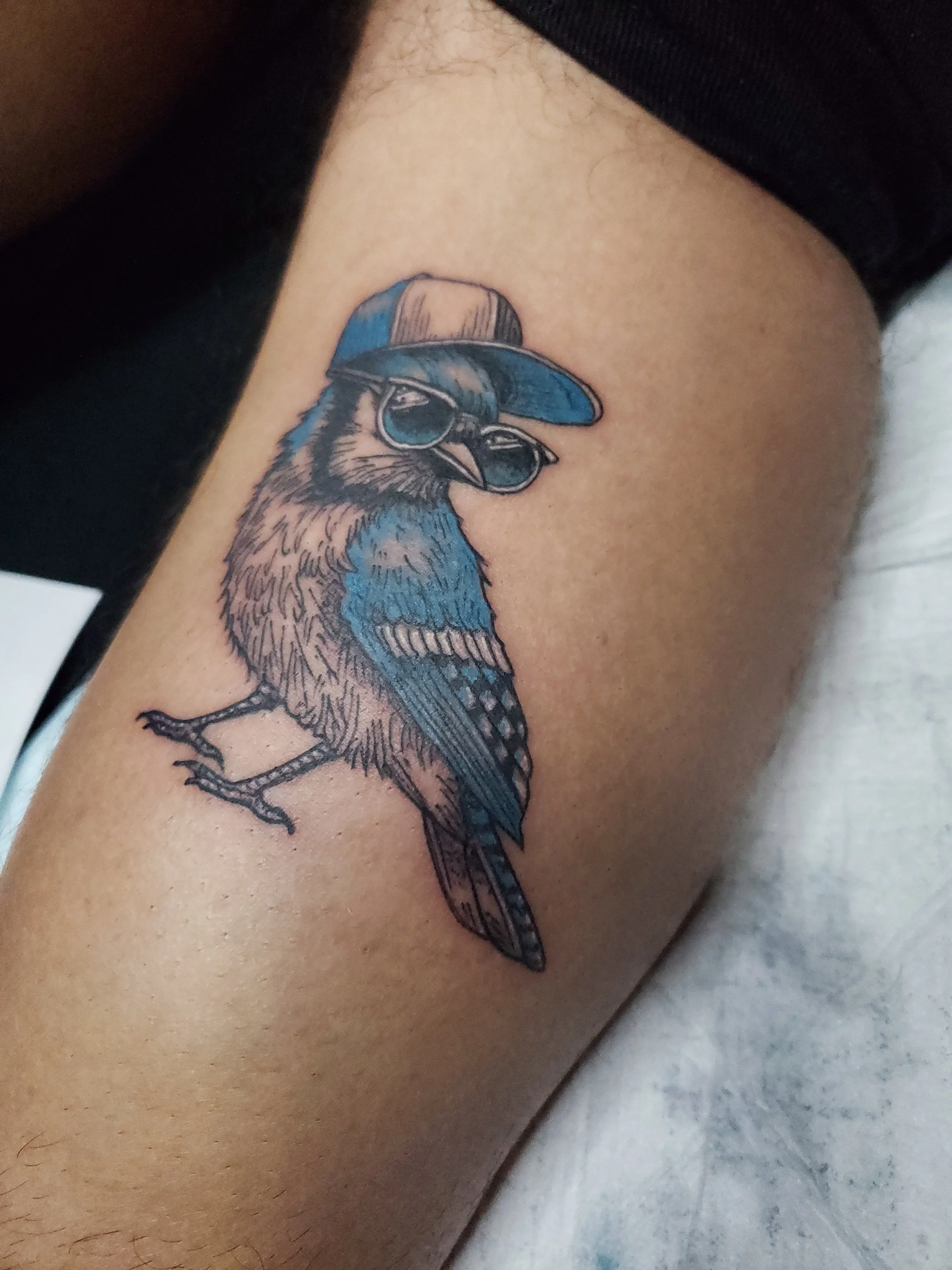Tattoo of a bird wearing sunglasses and a cap on person's thigh.