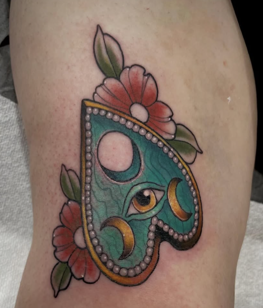 Colorful tattoo of a heart with an eye in the center, surrounded by flowers and leaves.