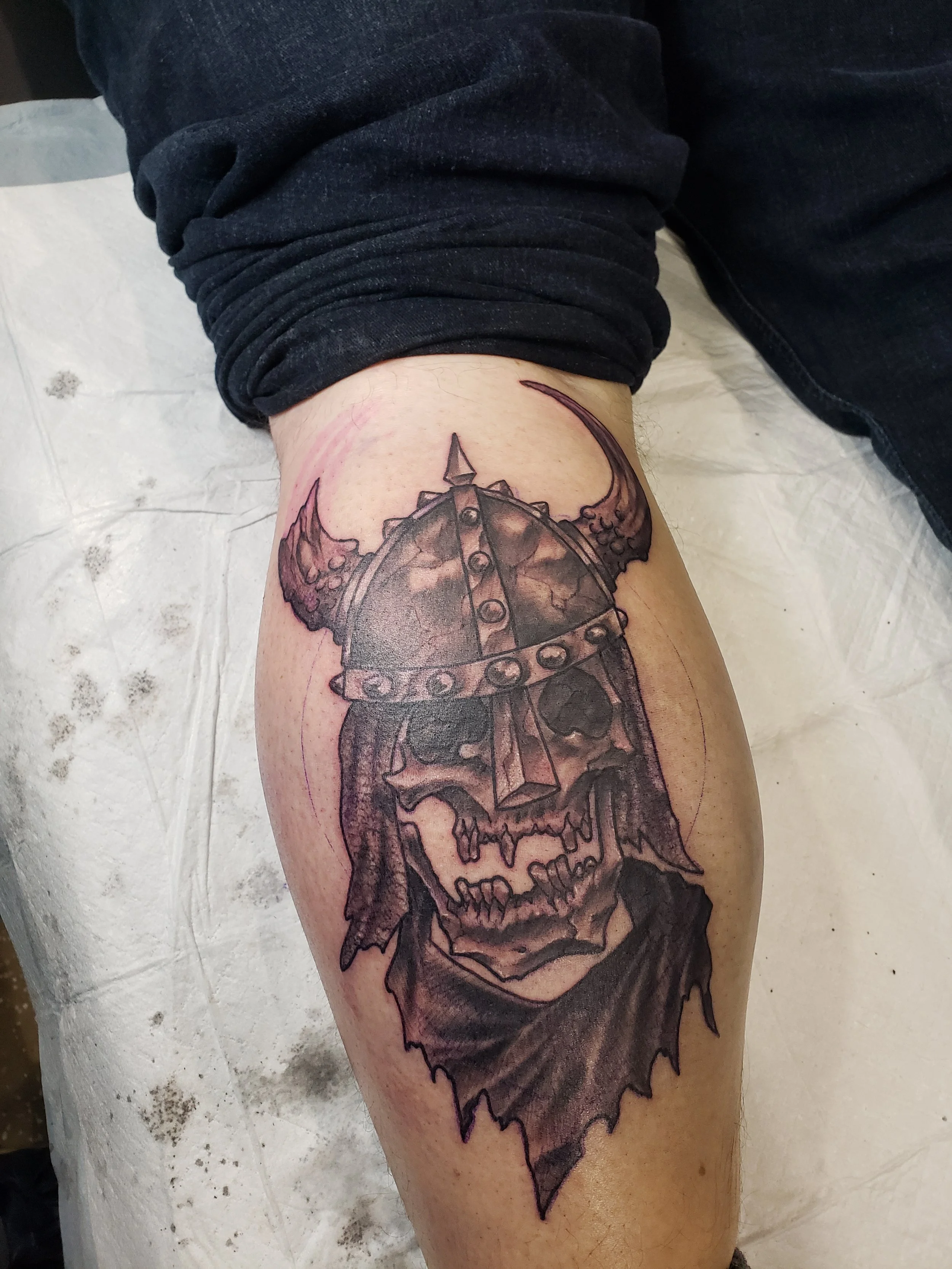 A tattoo of a detailed skull on a person's thigh, with elements resembling a mechanical or steampunk design.