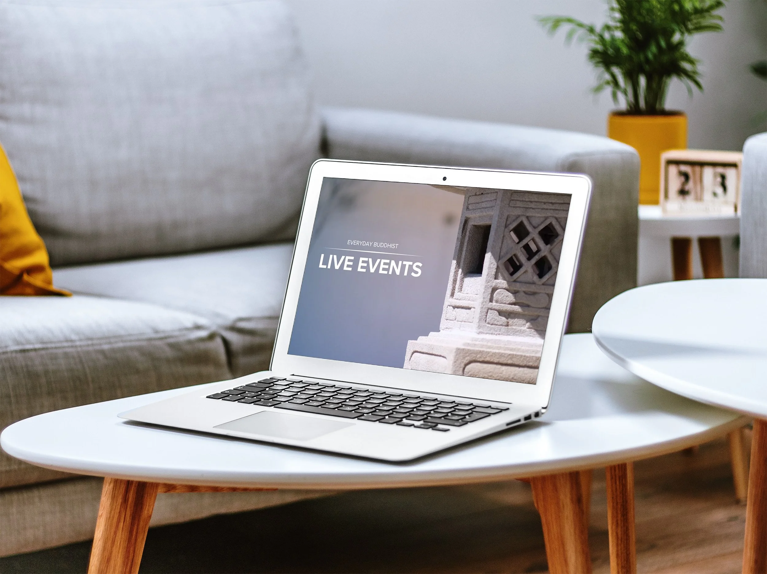 A laptop sits on a white table that shows the intro screen of Everyday Buddhist live events.