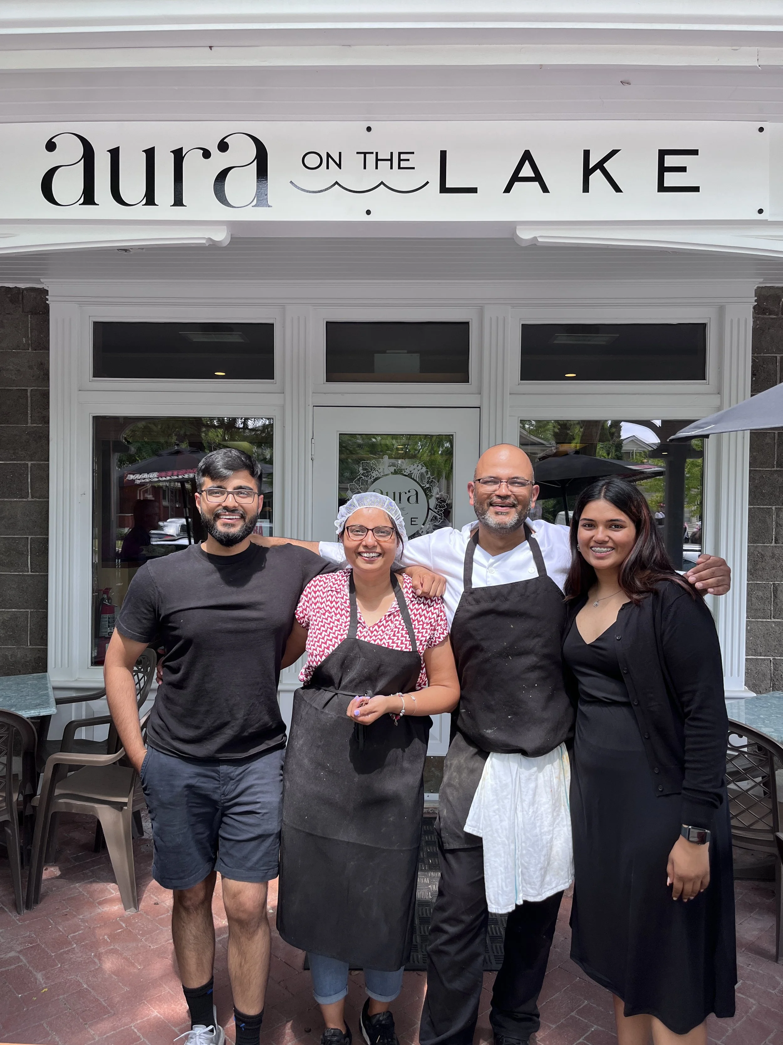 Group of four people standing outside Aura on the Lake restaurant, smiling, with two men in chef uniforms and two women in casual attire.