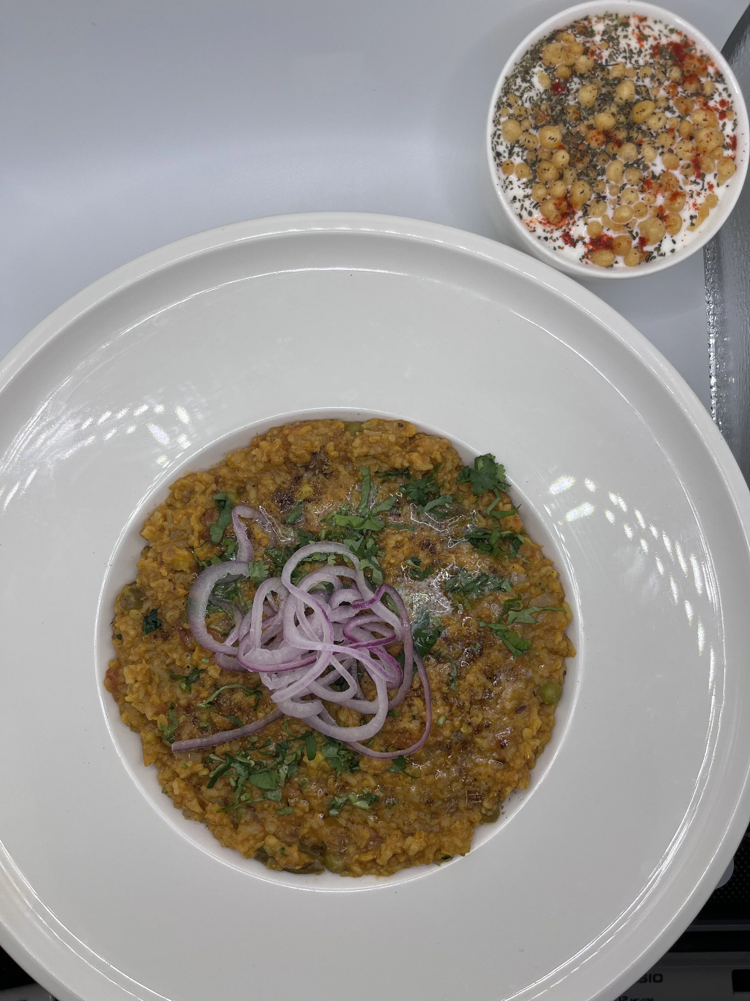 A plate of spicy lentil stew garnished with sliced red onions and herbs, accompanied by a bowl of yogurt topped with chickpeas, herbs, and spices.