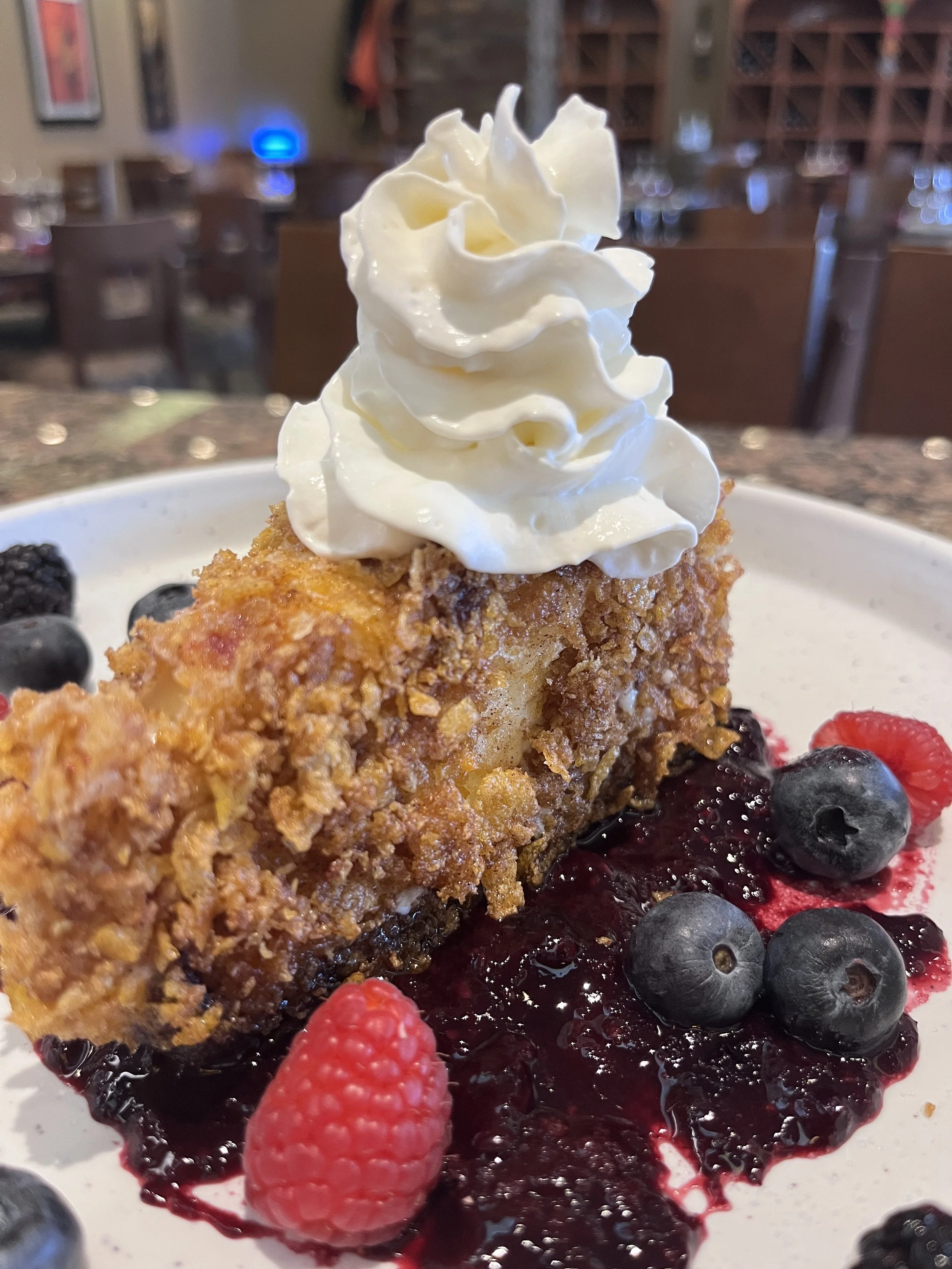 Fried dessert with whipped cream topping, berries, and berry sauce on a plate.