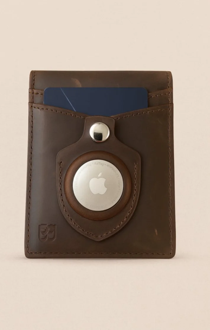 Brown leather wallet with built-in AirTag holder, metal button flap, and visible blue card, shown on a neutral background.