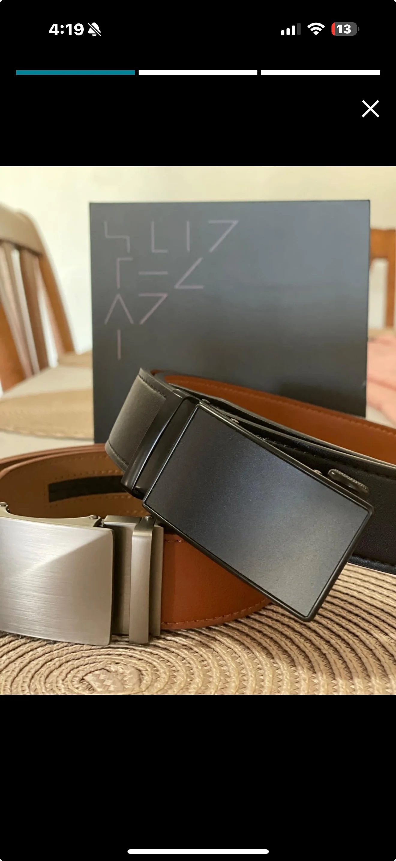 Two ratchet belts with sleek buckles—one black, one brown—displayed with gift box on woven surface.