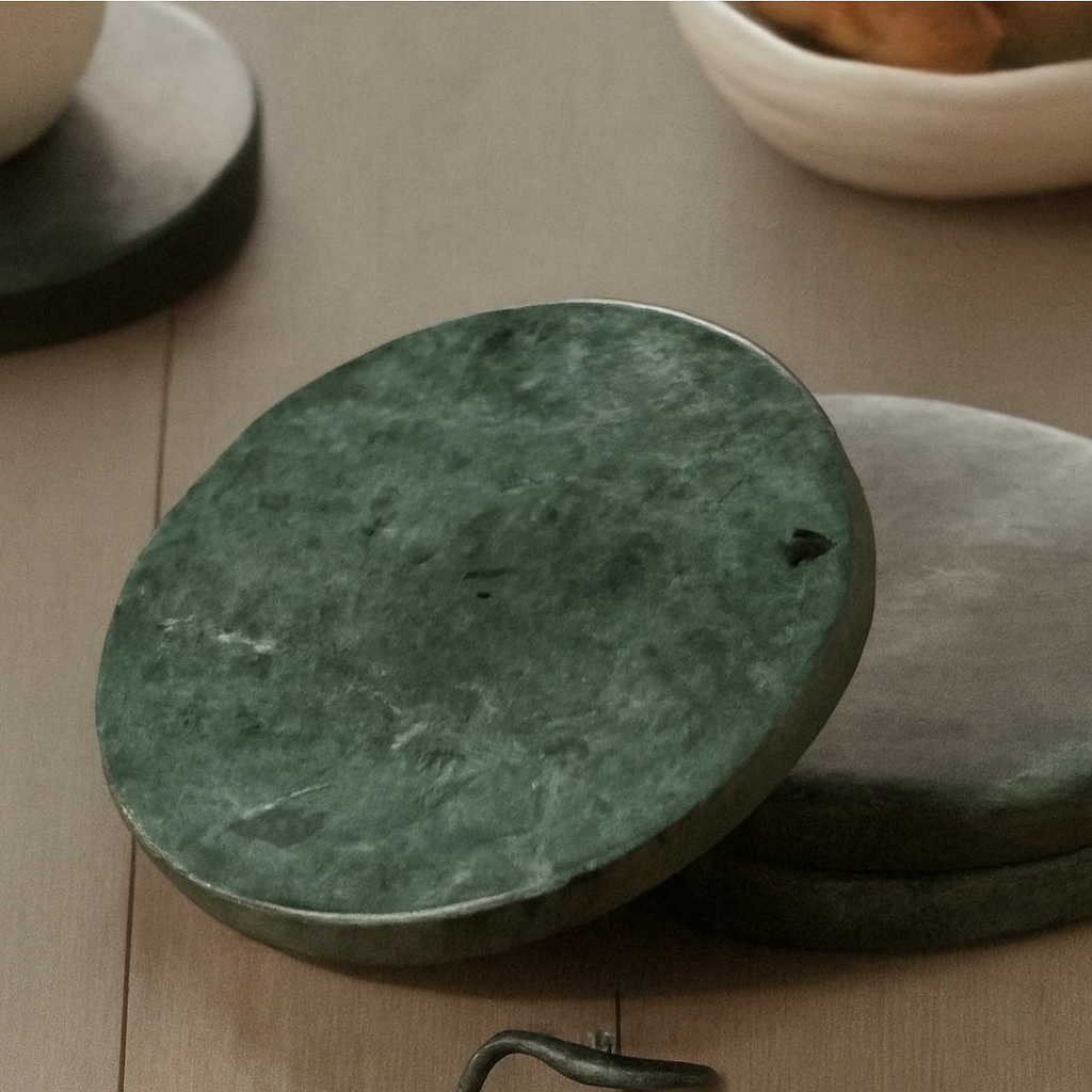 Green marble coasters on wood table with mug, toast, notebook, and glasses in a softly lit, cozy reading setup.