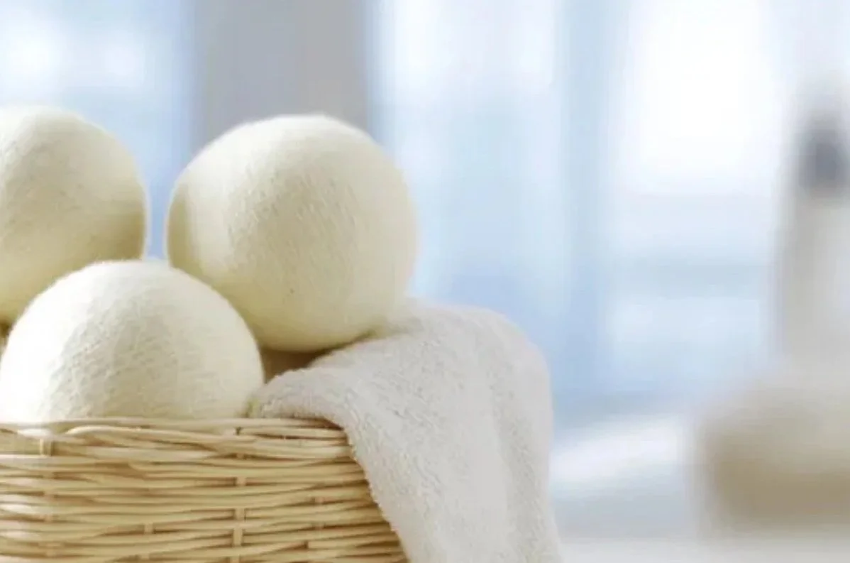 Cream-colored wool dryer balls in a wicker basket with a soft towel, set in a bright, clean indoor space.A