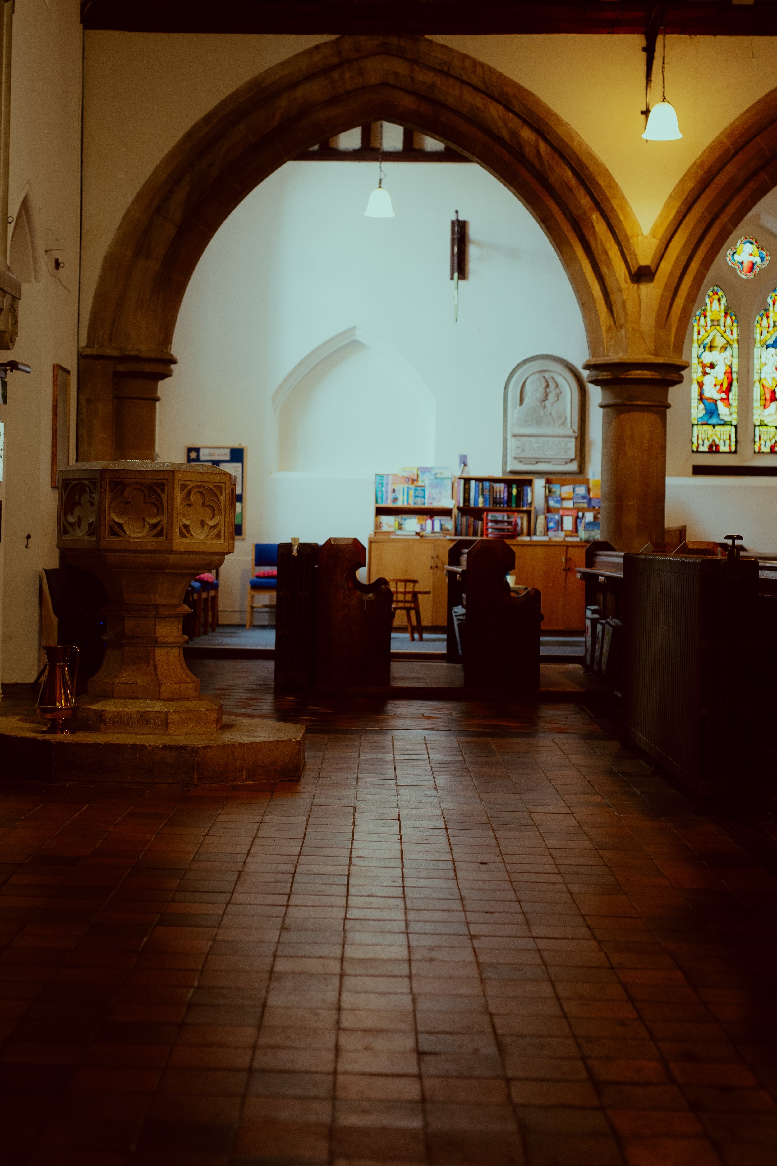 Interior of a church with wooden pews, stained glass windows, and a wooden pulpit, illuminated by hanging lights.