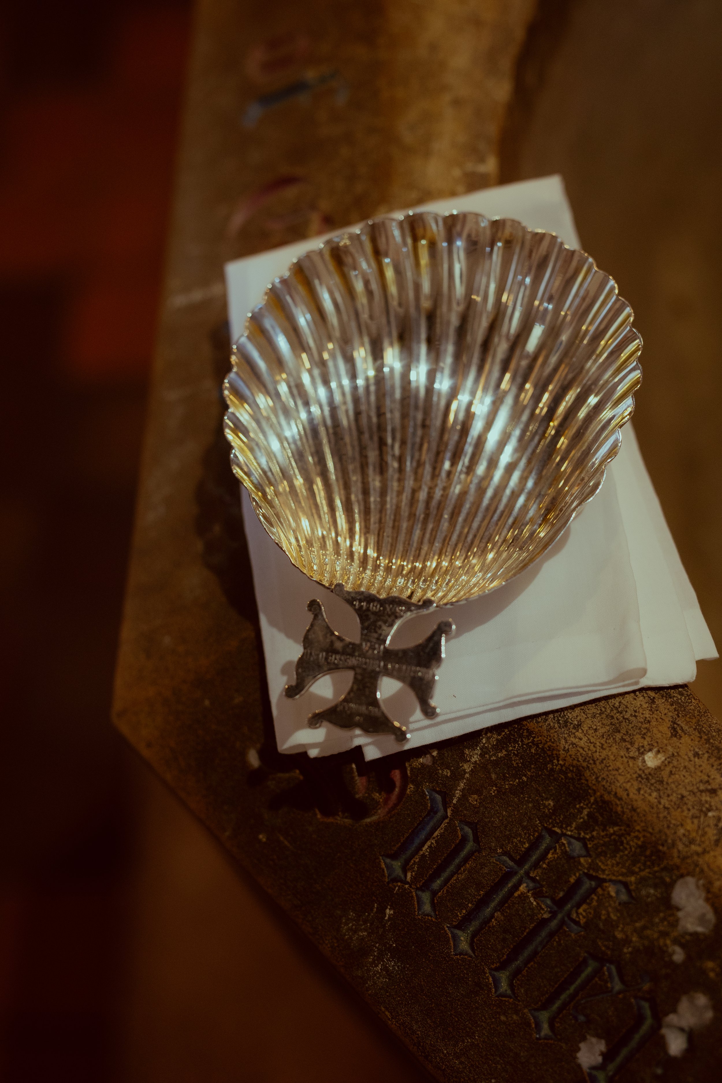 A decorative silver shell-shaped dish with a black ornate stand, placed on a white napkin on a rustic wooden surface.