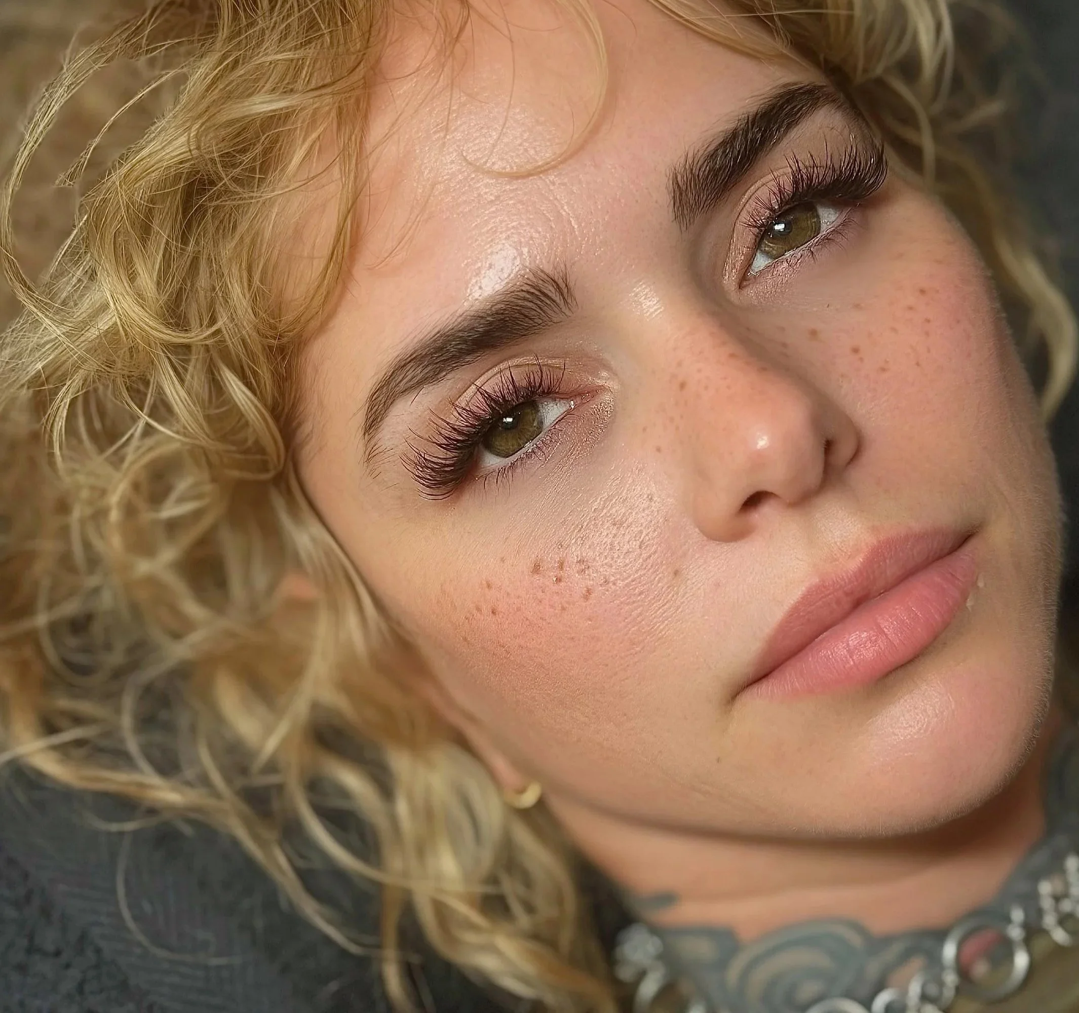 Close-up of a person's face, highlighting green eyes, long eyelashes, light skin with freckles, and curly blonde hair.