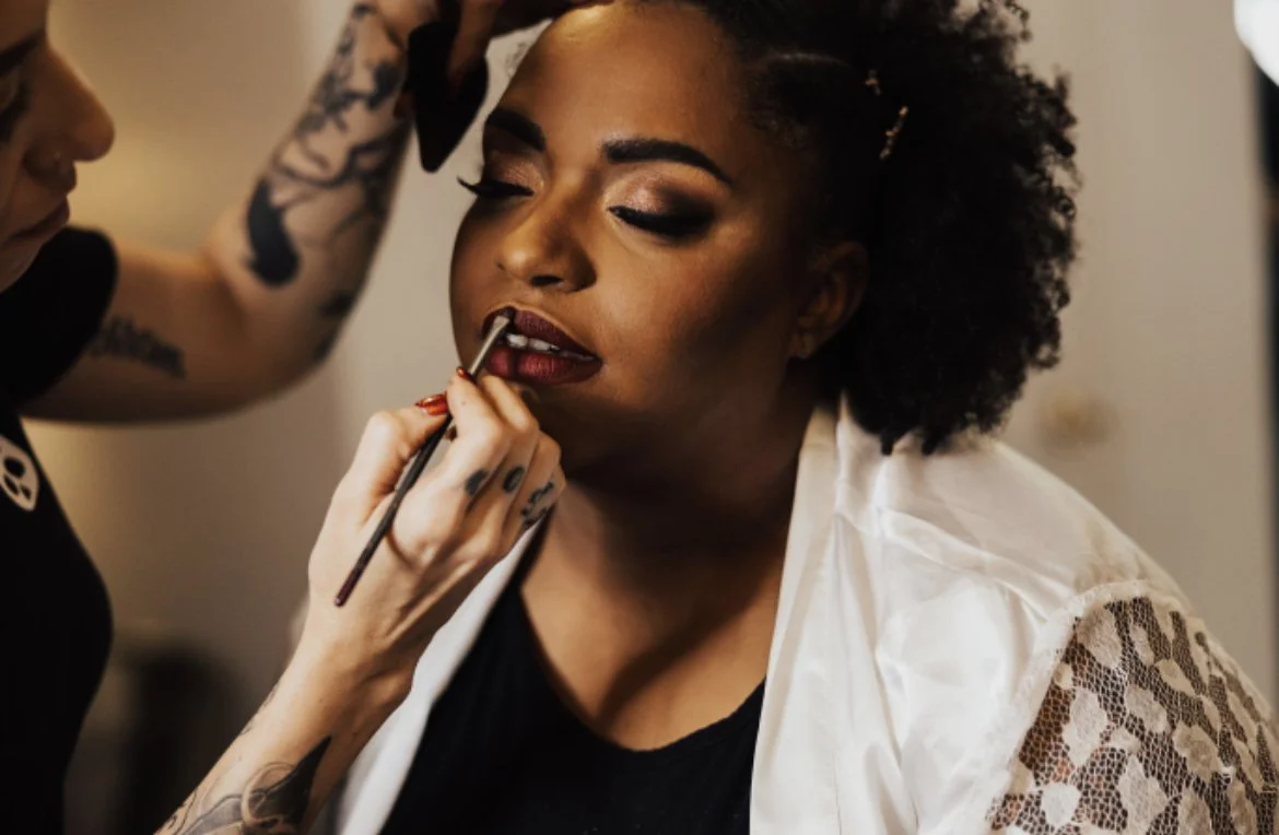 Makeup artist applying lipstick to woman with curly hair in a beauty salon.