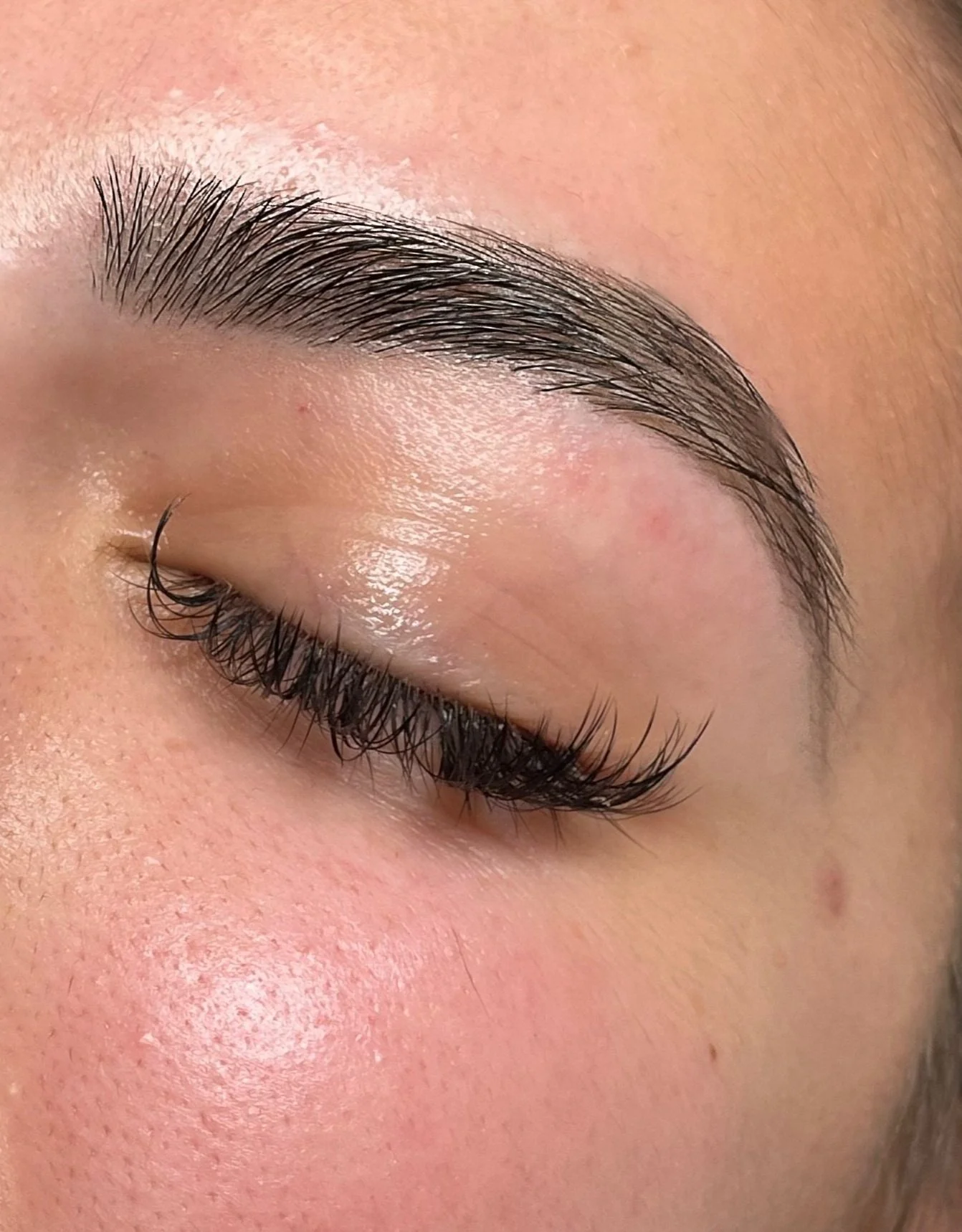 Close-up of a person's closed eye, showing natural eyelashes and eyebrow, with smooth skin around the eye.