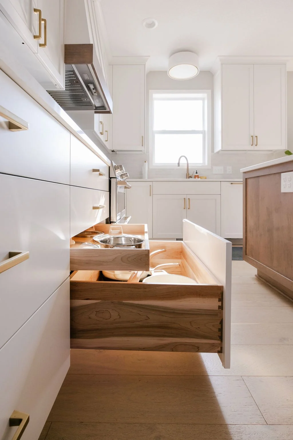 Modern custom kitchen with white shaker cabinets, brass hardware, light wood flooring, and a built-in pull-out drawer designed for pet food and water bowls.