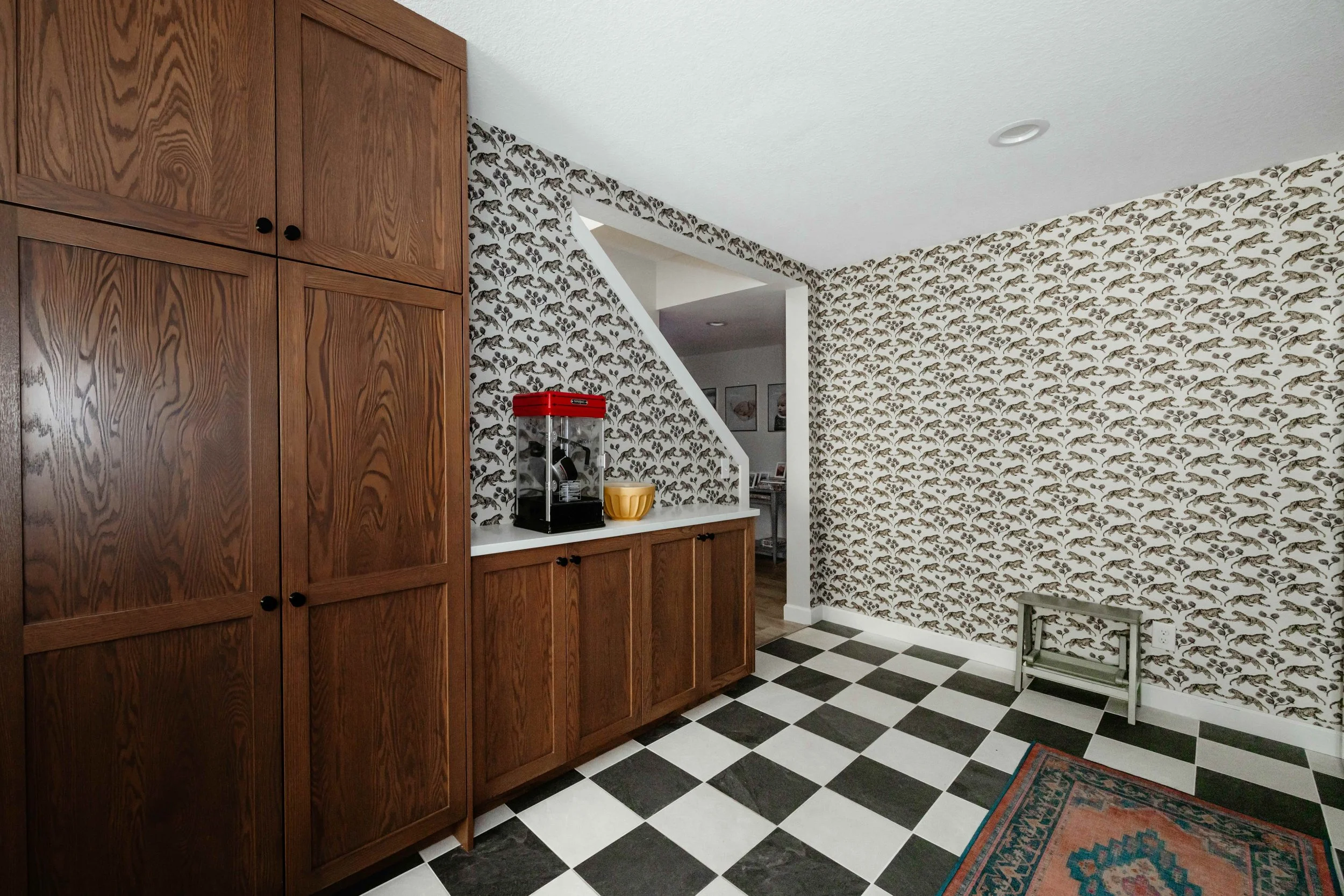 a photo of red oak cabinetry, tiger grasscloth wallpaper by Sarah Sherman Samuel and large checkerboard floor tile and Sunset Bazaar Tropic Coral Flatwoven Rug