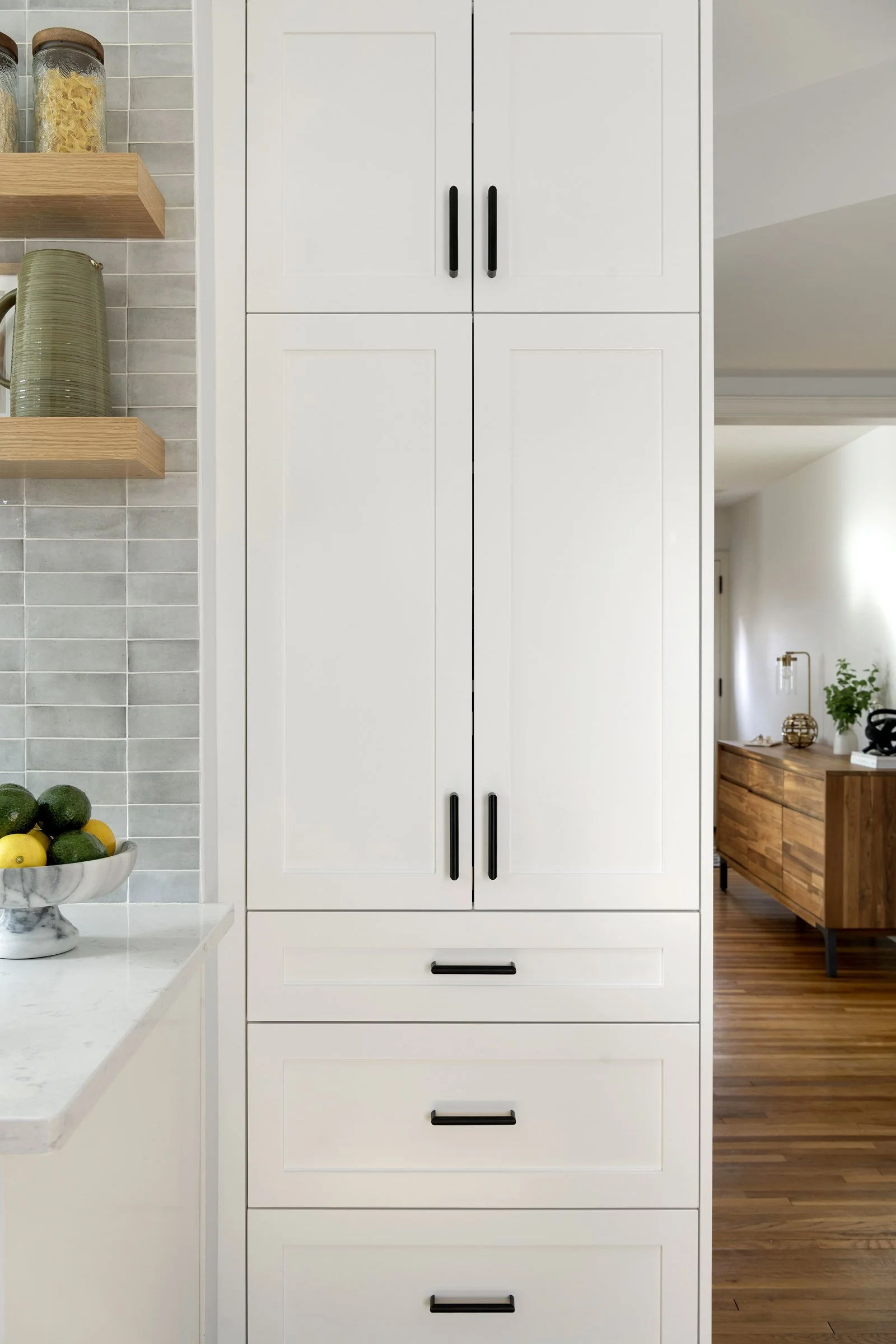 Tall white kitchen cabinets with black hardware and integrated drawers in a modern layout.