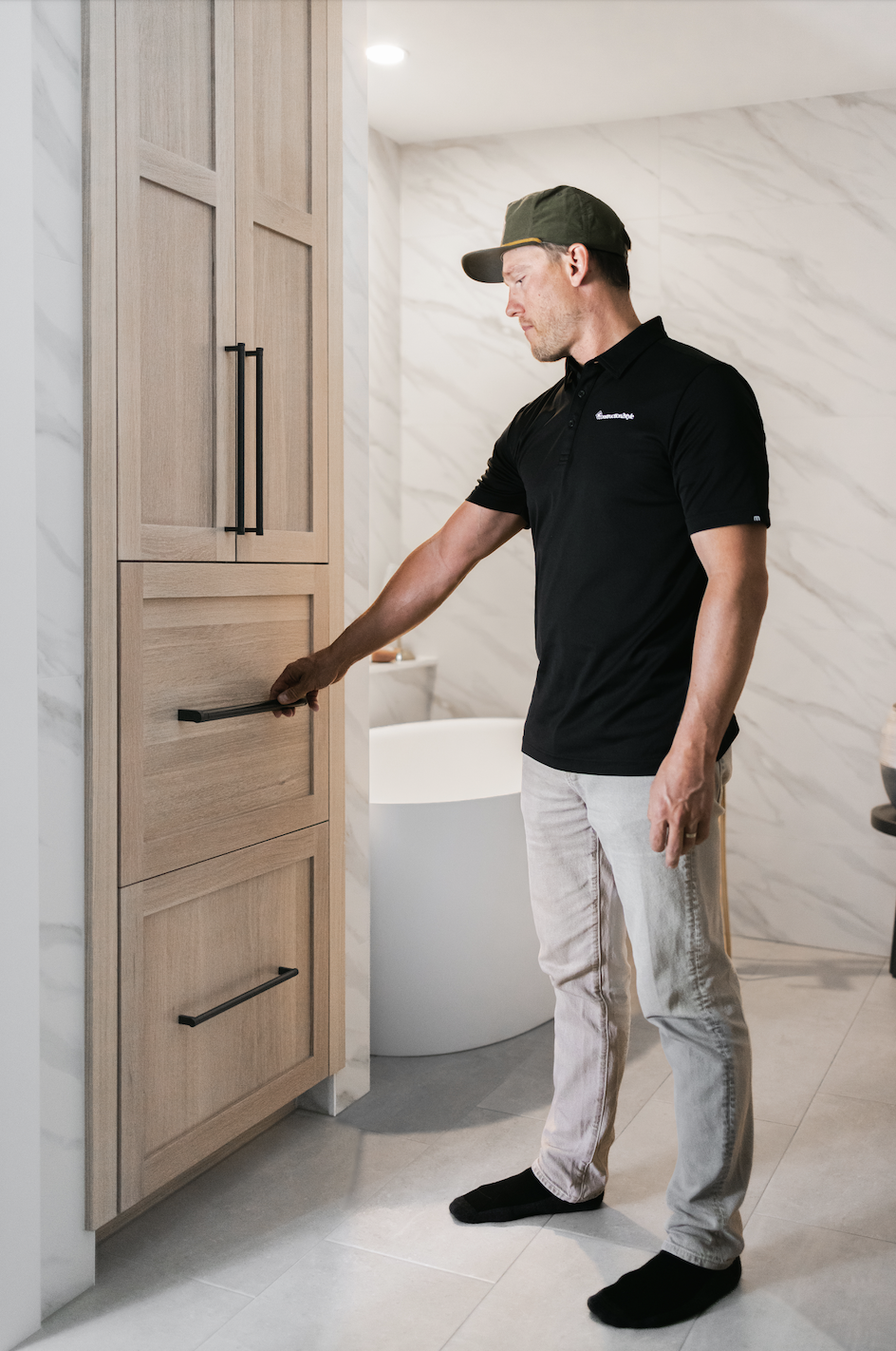 Man opening middle drawer on tall light wood bathroom cabinets