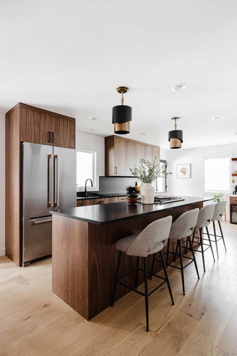 Modern kitchen with walnut cabinets, large island with black countertop, and upholstered bar stools.