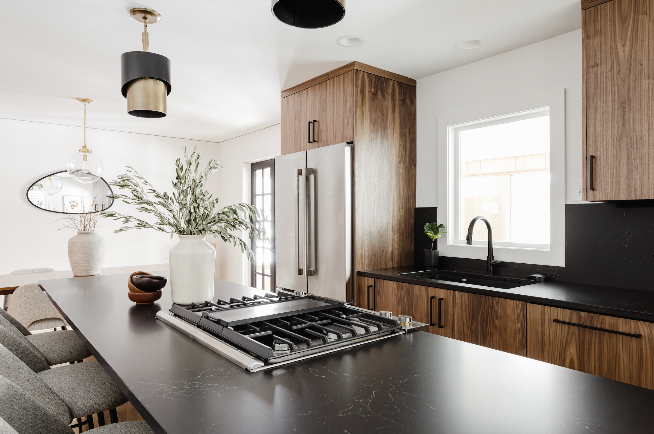 Perspective shot of custom-grain walnut cabinetry and integrated refrigerator panels, highlighting a black quartz island with a stainless steel range and matte black sink fixtures.