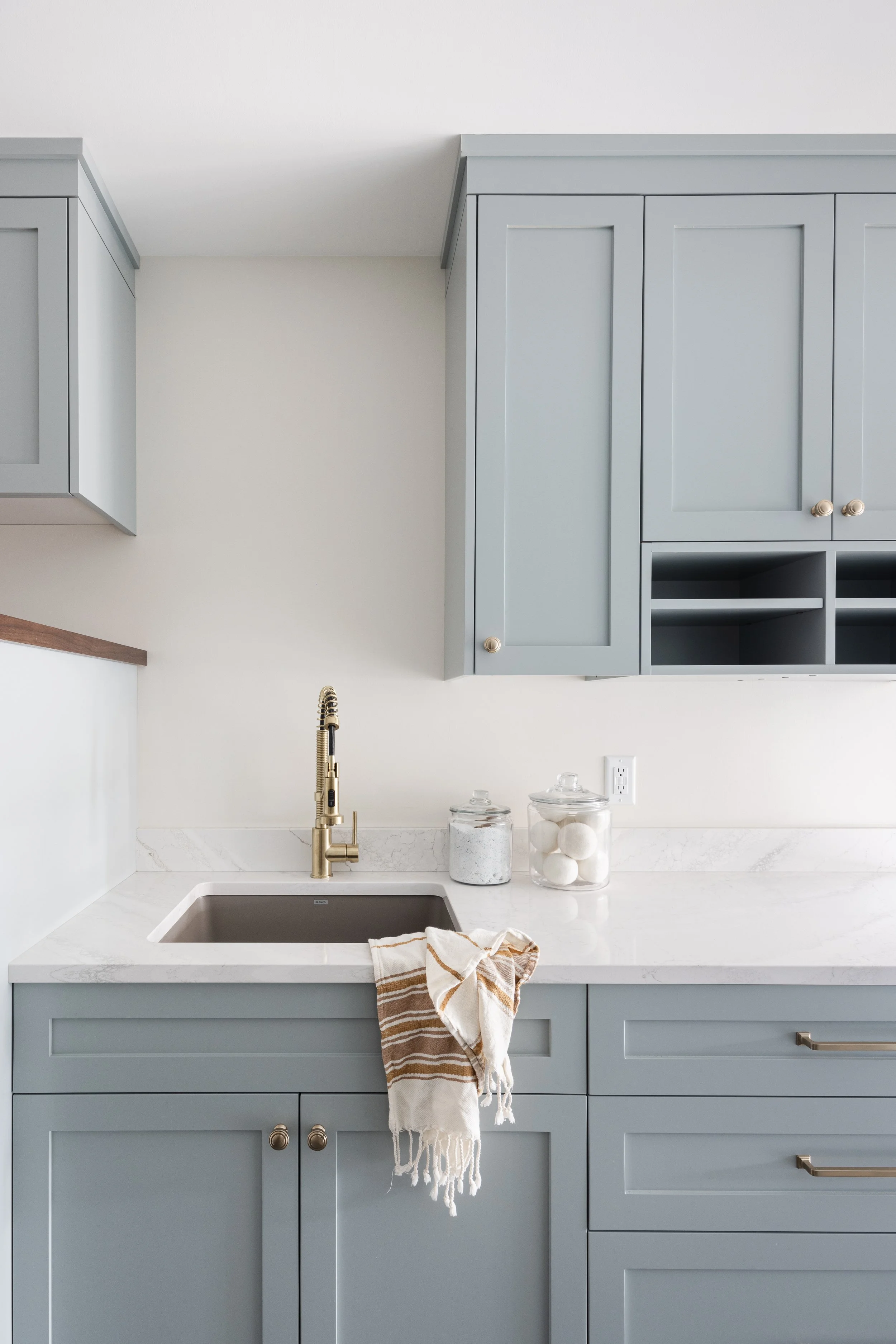 Light blue custom shaker cabinets with brass hardware, white quartz countertops, and a gold pull-down faucet in a modern laundry room