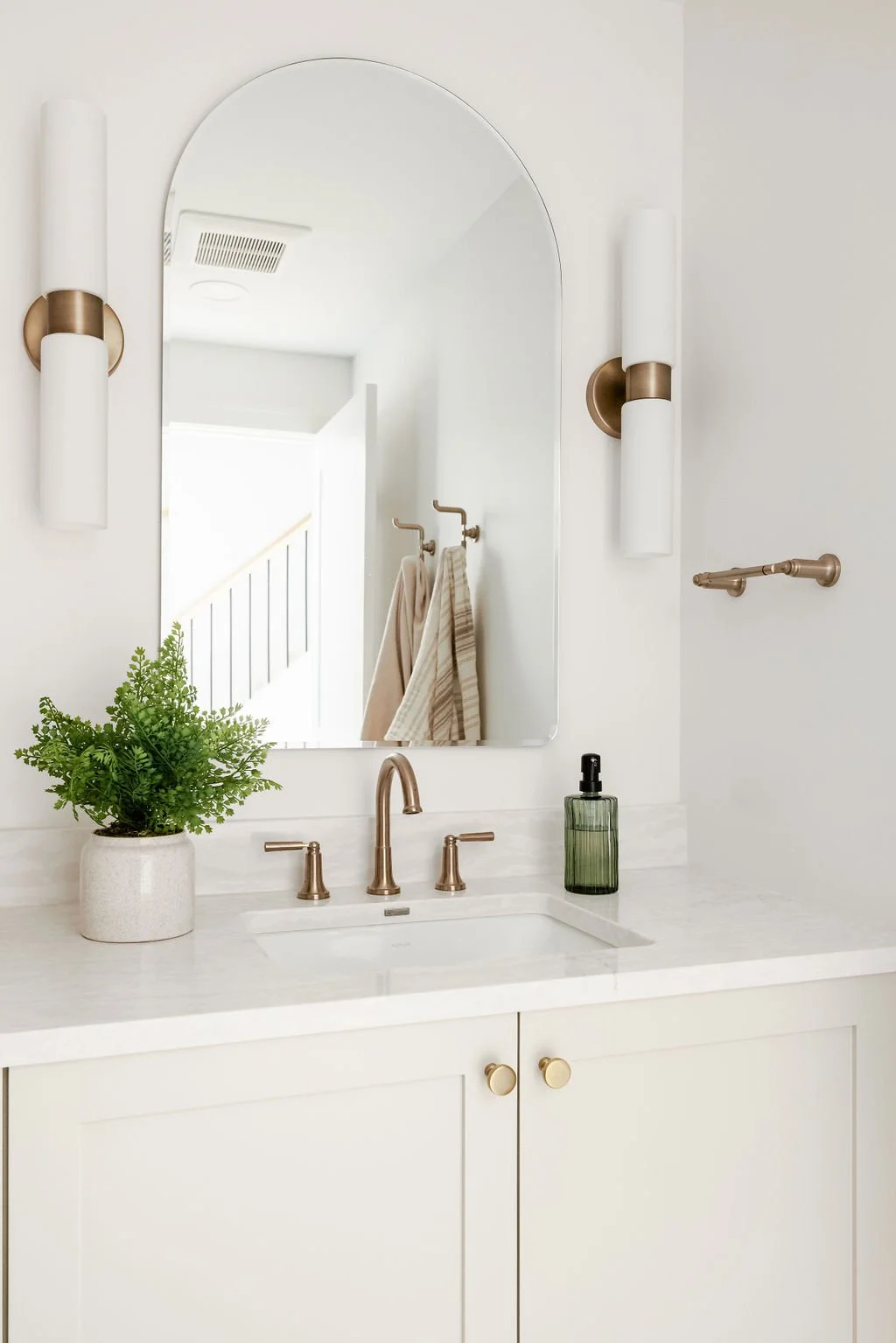 Minimalist bathroom vanity with white cabinetry, warm brass accents, arched mirror, and soft neutral styling.