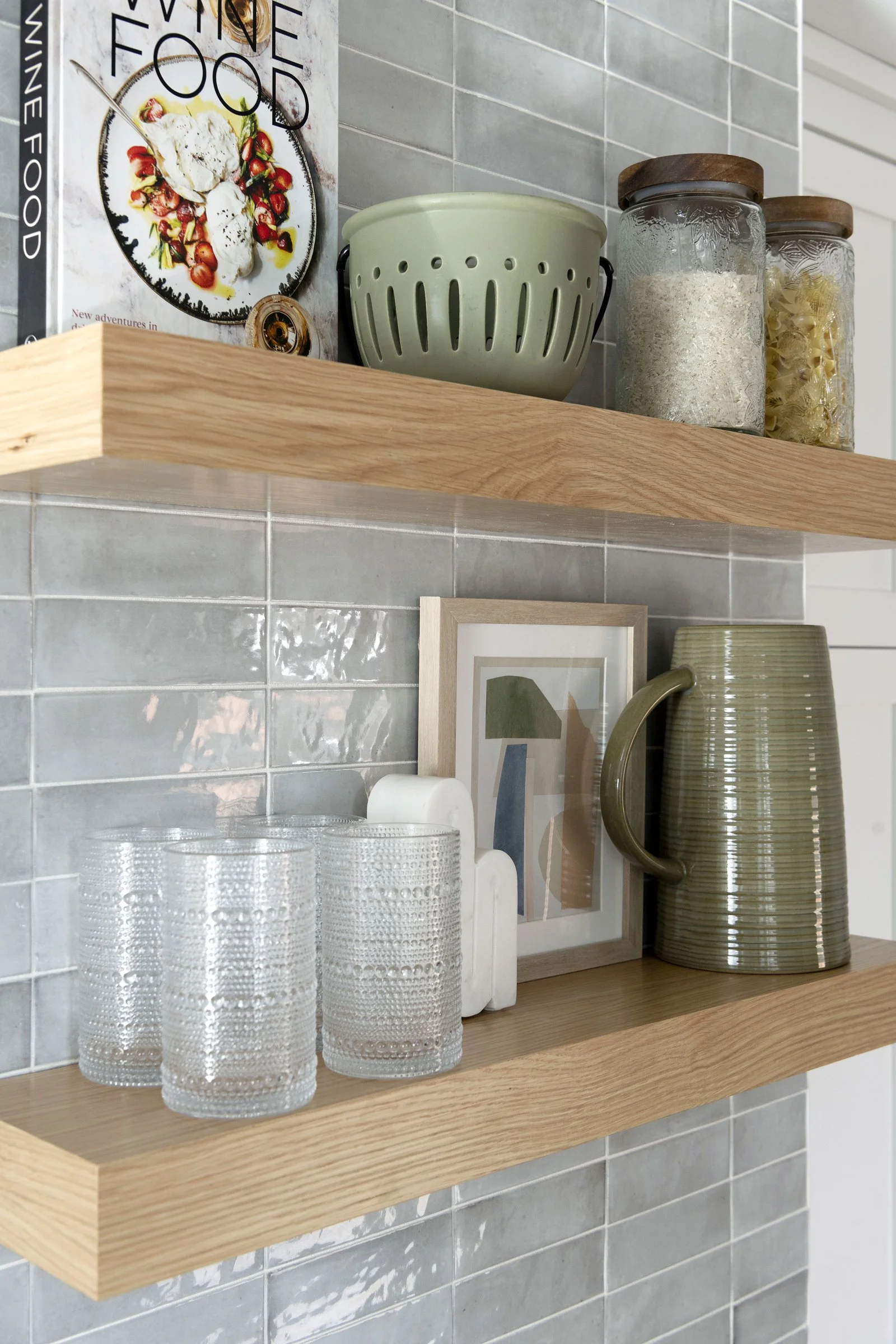 Open wood shelving styled with glassware, jars, and decor against a tiled backsplash.