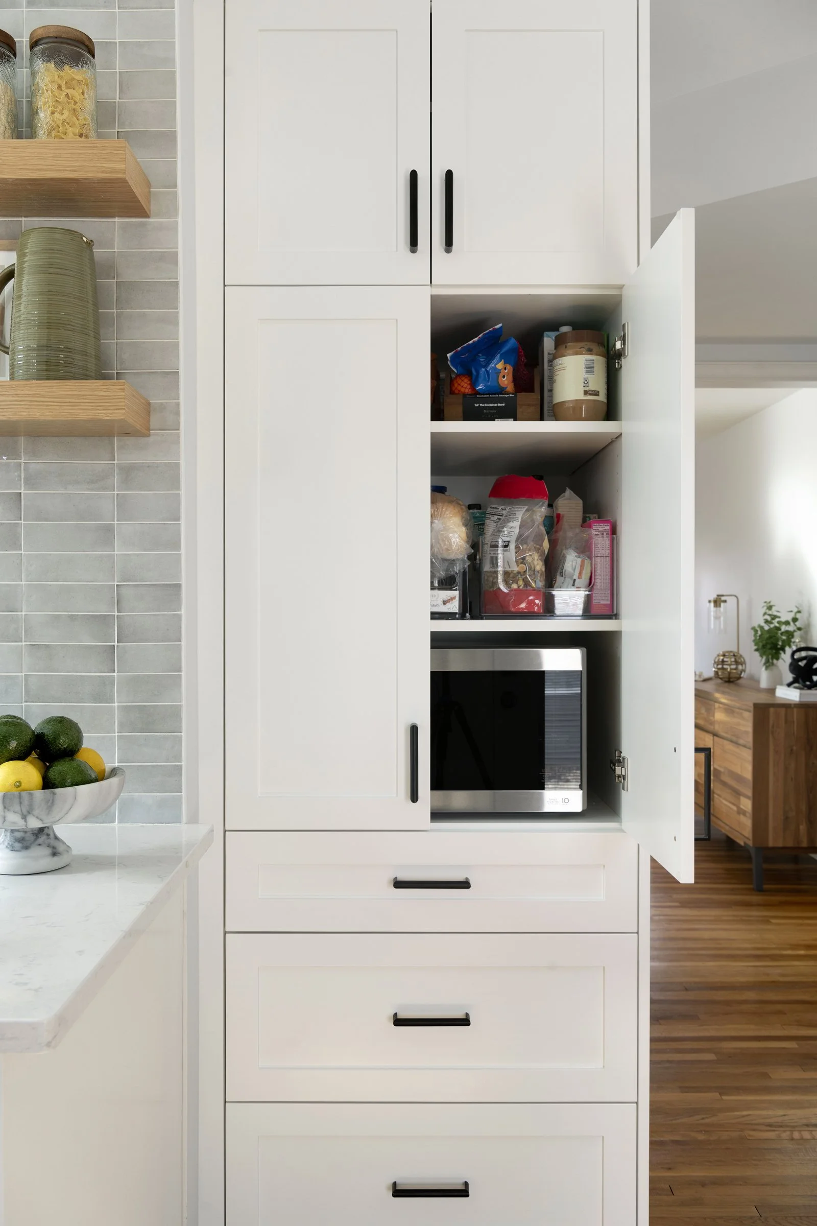 Tall white cabinets with open pantry storage and a built-in microwave, showcasing an organized interior space.