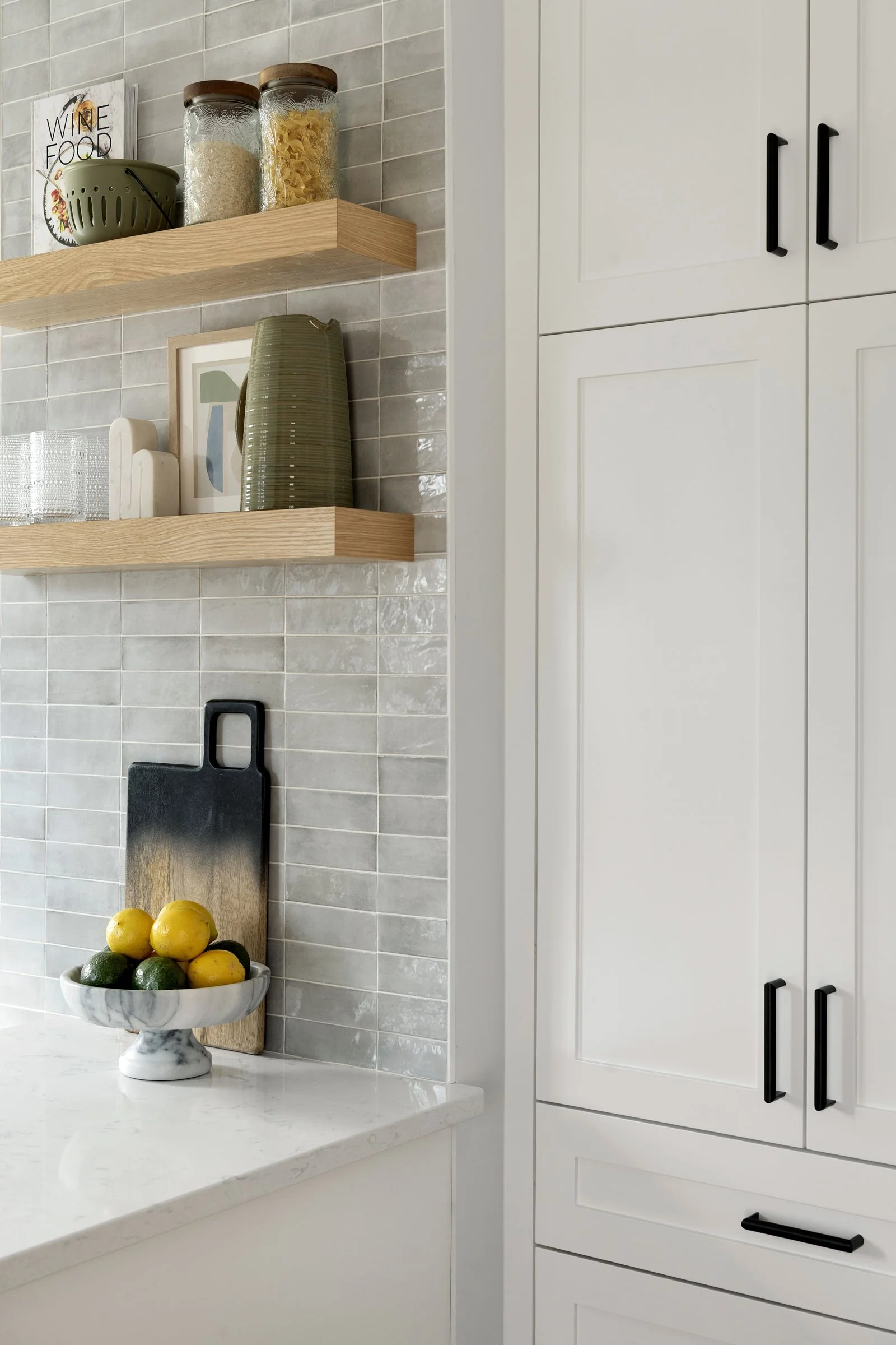 Close-up of white cabinets with black pulls, open wood shelving, and tiled backsplash detail