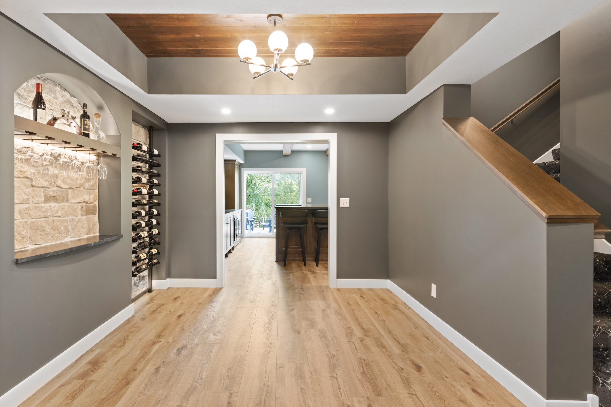 Living space with custom built-in wine racks, stone display shelving, stairs, and wood flooring, leading to a bar area with cabinetry.