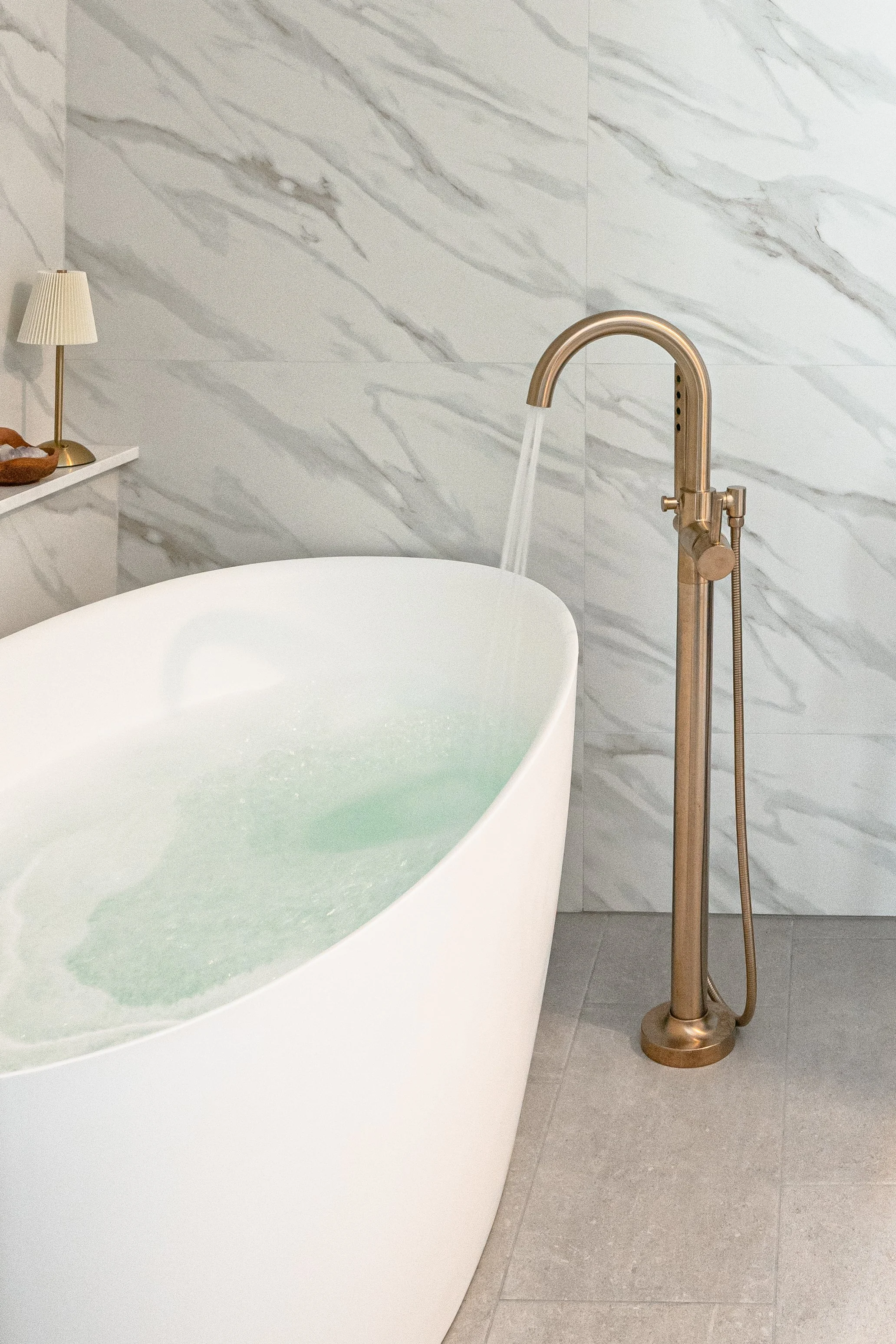 Freestanding tub with brass faucet beside light wood bathroom cabinets