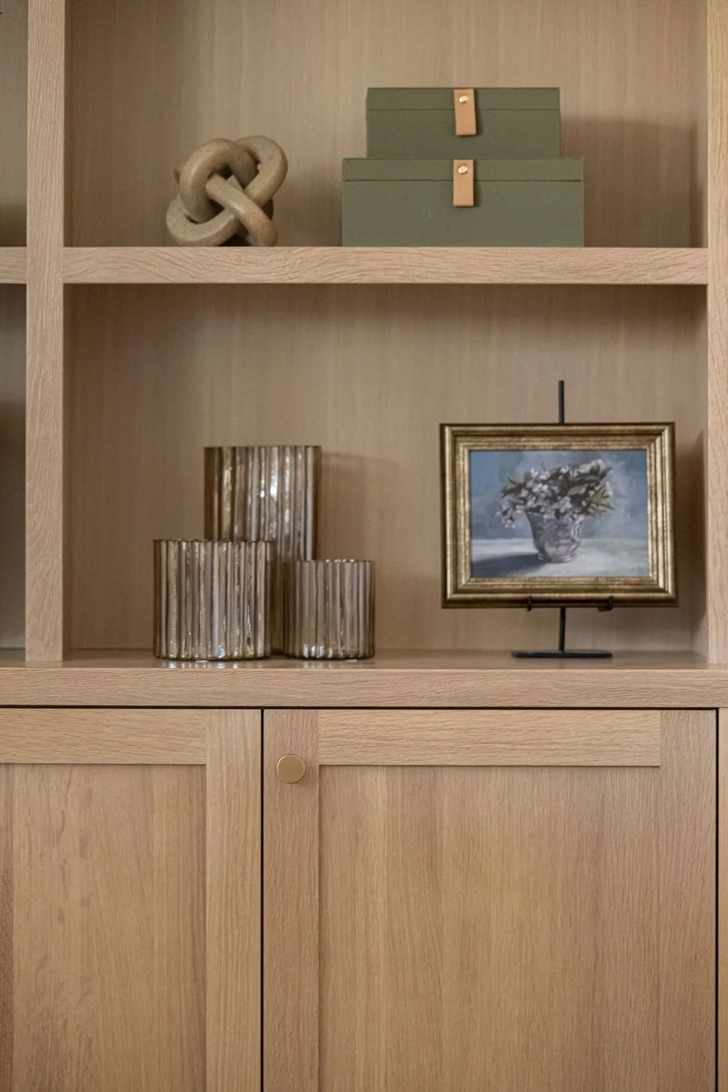 Styled wood shelving with layered decor including green boxes, textured glass pieces, and framed artwork.